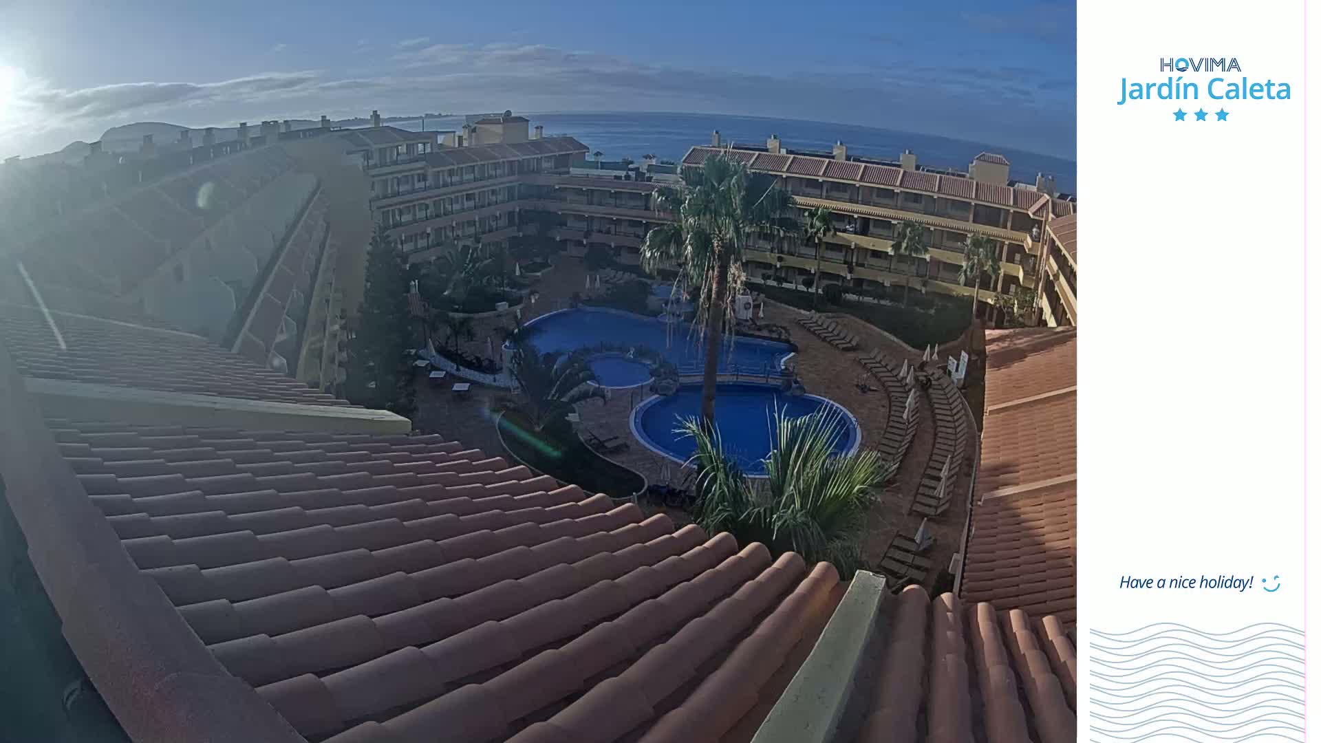 A sunny day reveals a resort with multiple pools surrounded by buildings and palm trees, overlooking a calm ocean.