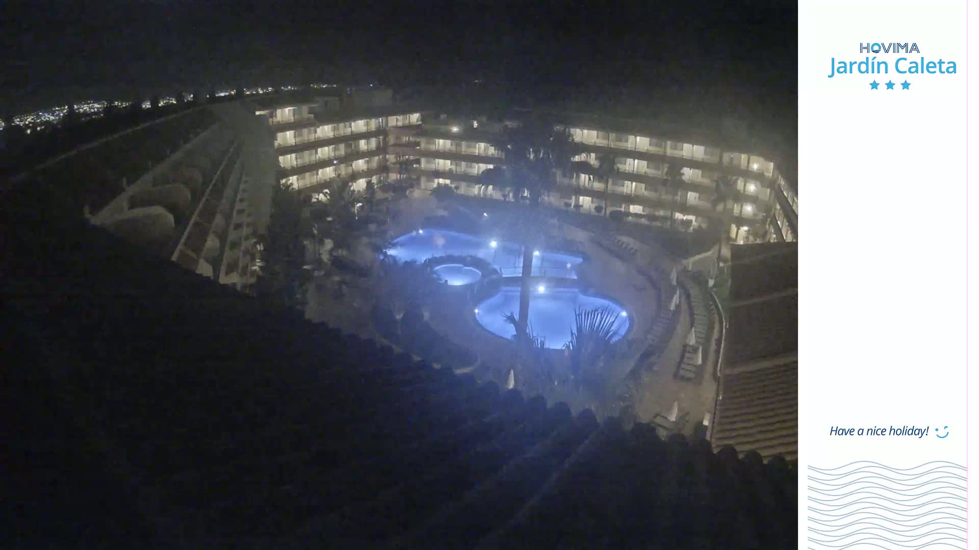 A nighttime overhead view shows a multi-story building surrounding a lit-up swimming pool complex.