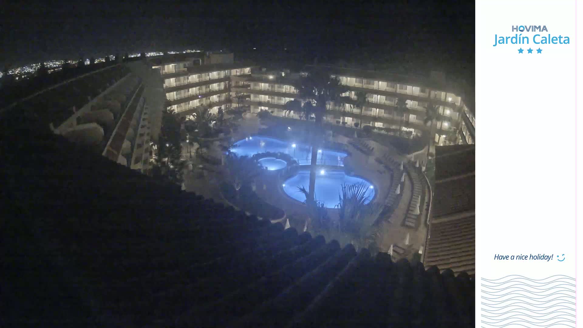 A nighttime, high-angle view shows a multi-story building complex surrounding a lit pool area.