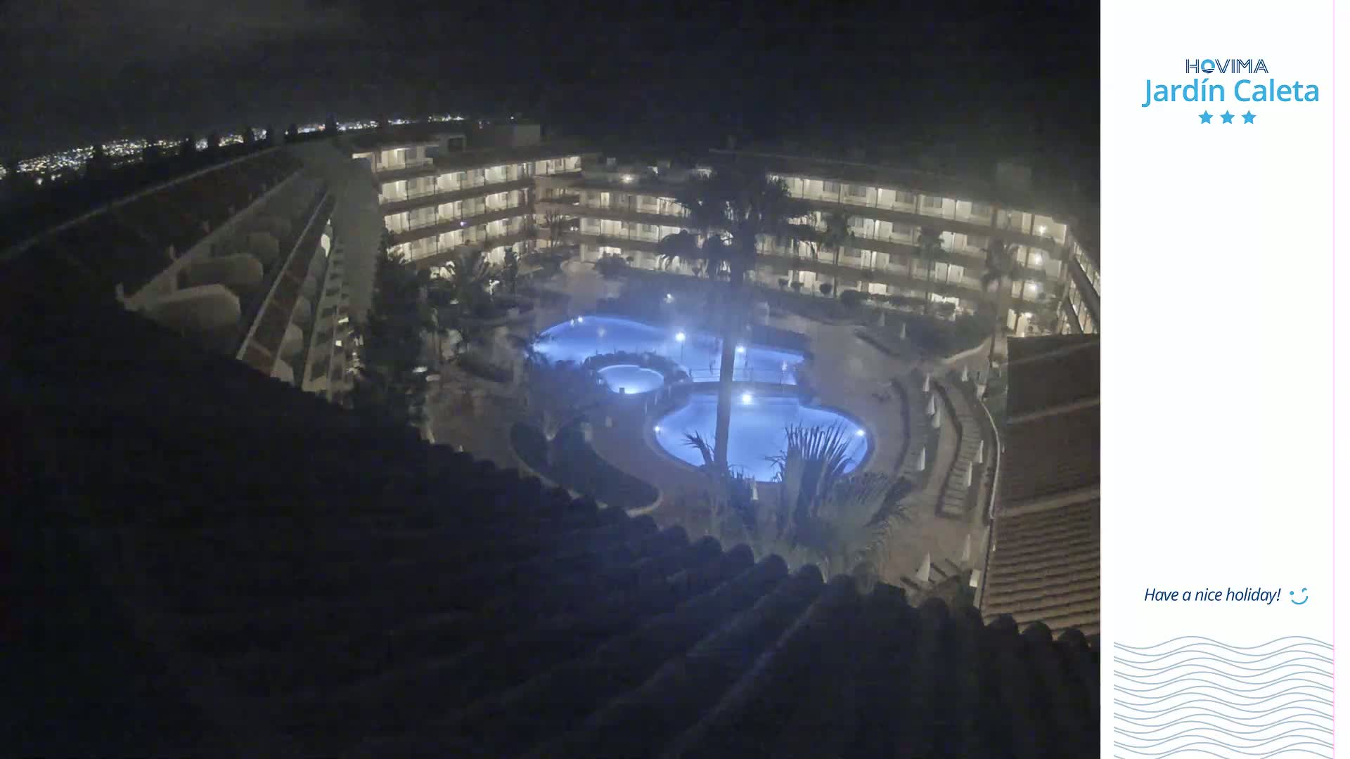 A nighttime, high-angle view shows a multi-story building complex surrounding a lit swimming pool.