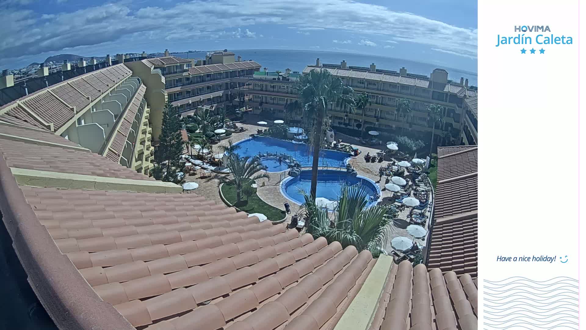 A sunny day overlooks a resort with multiple pools surrounded by tan buildings and palm trees.