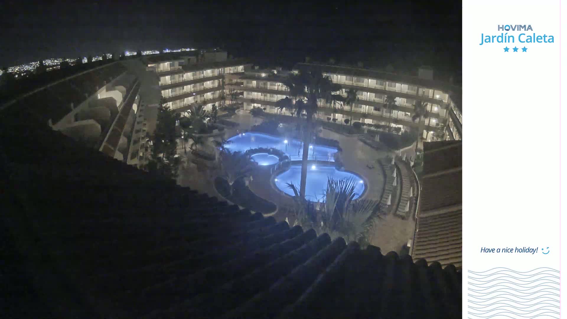 A nighttime, high-angle view of a multi-story hotel complex with a lit swimming pool in the courtyard.