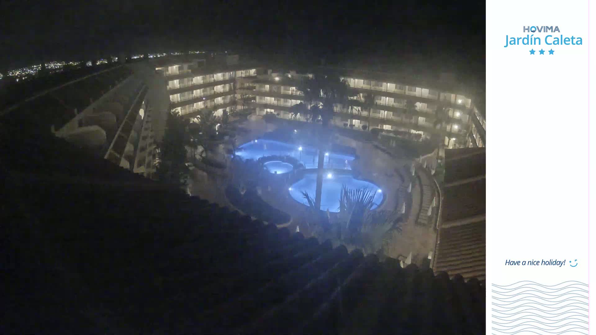 A nighttime, high-angle view of a multi-story building complex surrounding a lit swimming pool.