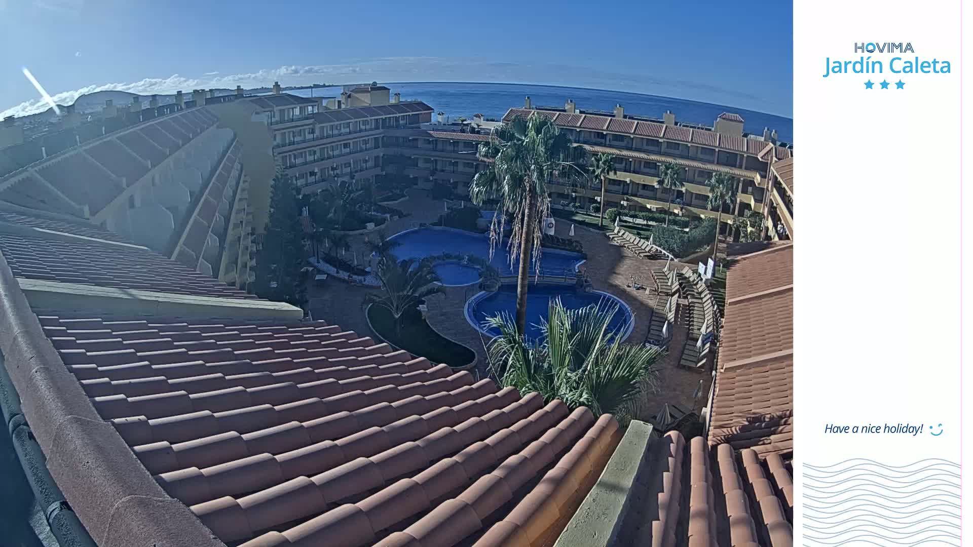 A sunny day overlooks a resort complex with a swimming pool and ocean views.