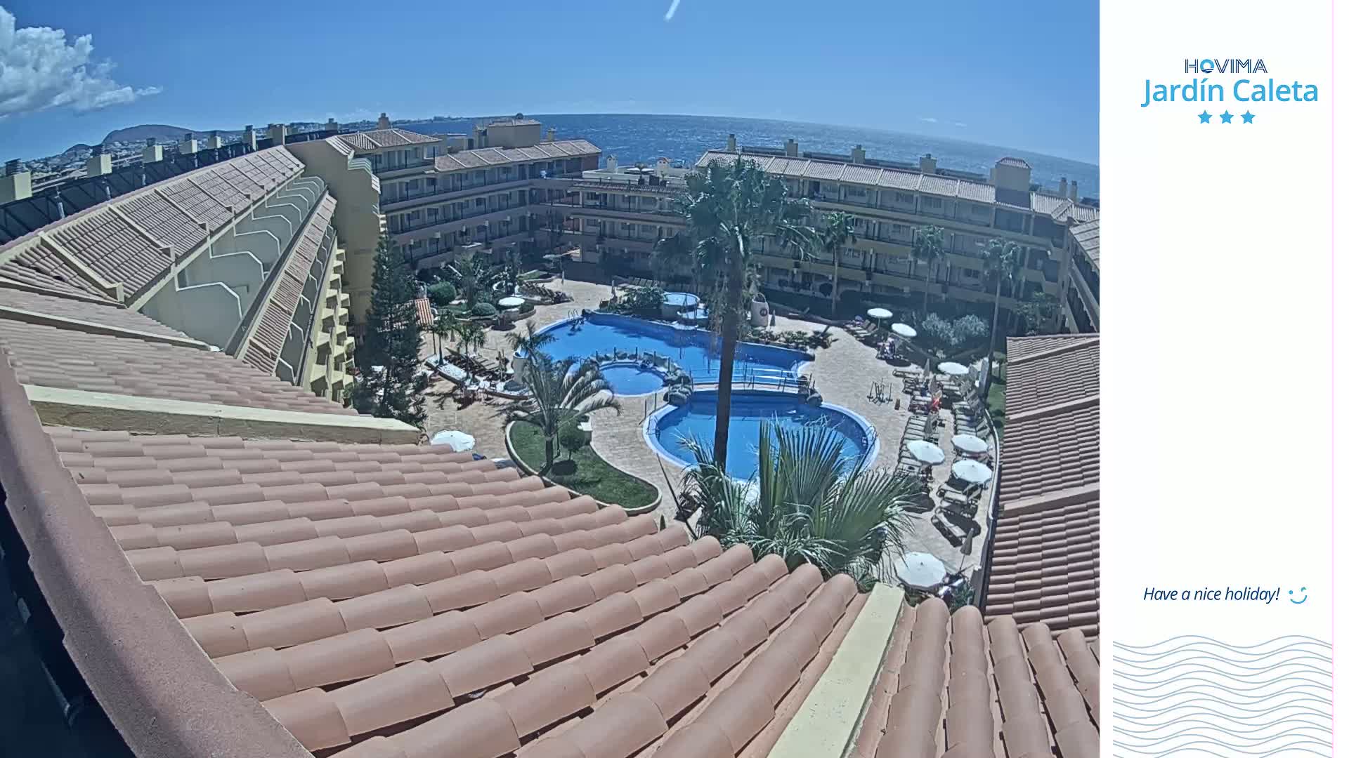 A sunny day overlooking a resort's courtyard with multiple swimming pools, surrounded by buildings and palm trees.