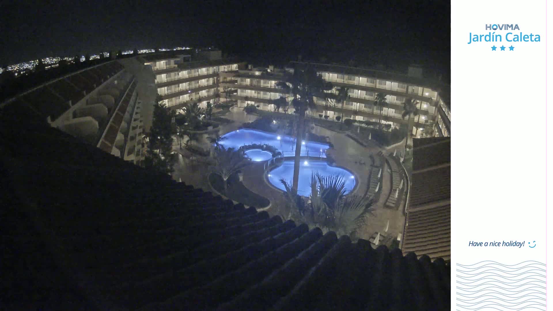 A nighttime aerial view shows a multi-story building complex surrounding a lit swimming pool.