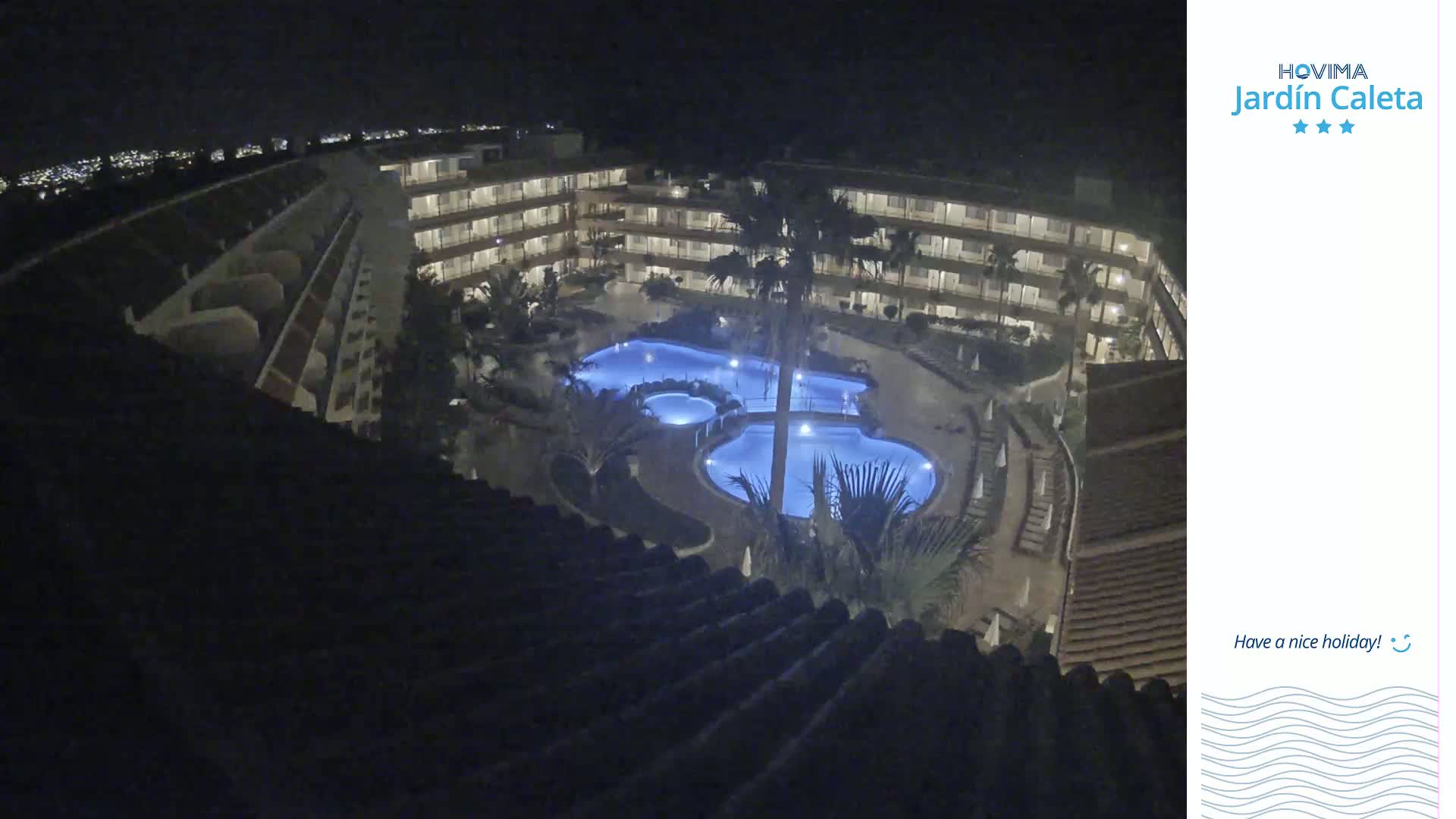A nighttime, high-angle view shows a multi-story building complex surrounding a lit swimming pool area.