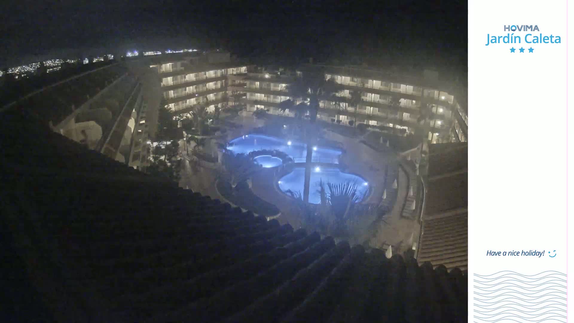 A nighttime, overhead view of a multi-story building with a lit swimming pool complex in the center.