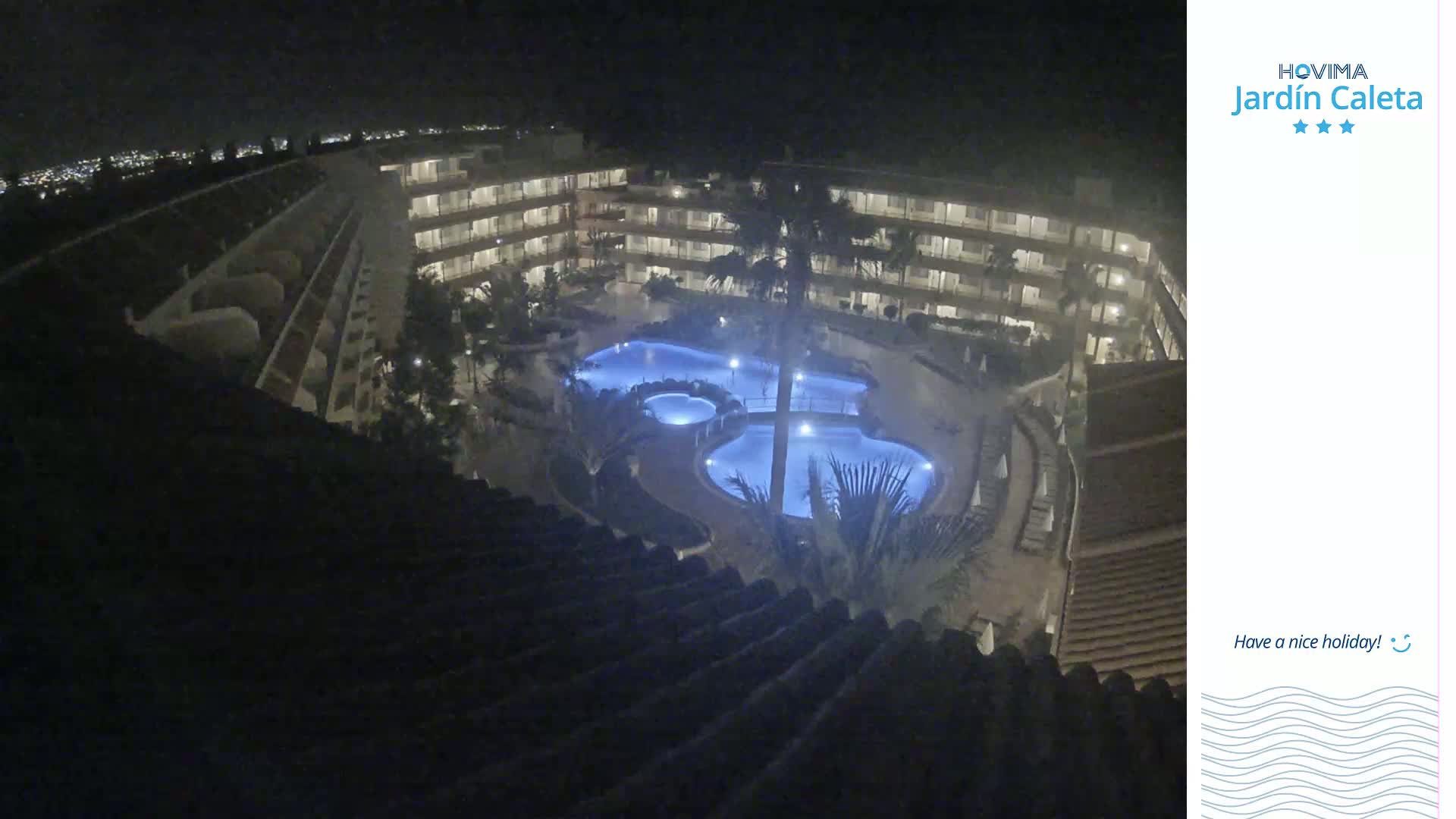 A nighttime view from a rooftop shows a multi-story building surrounding a lit swimming pool complex.