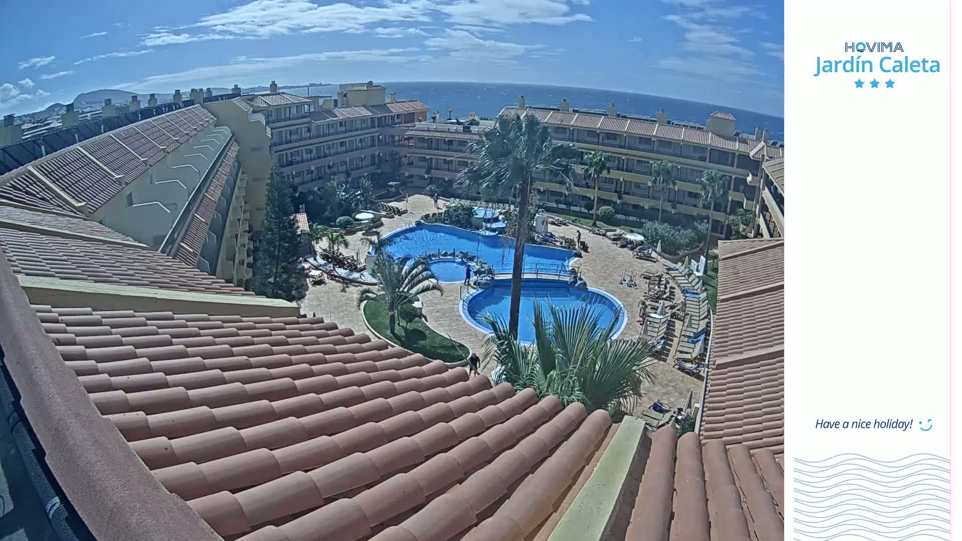 An overhead view of a resort complex with a large pool and surrounding buildings on a sunny day, overlooking the ocean.