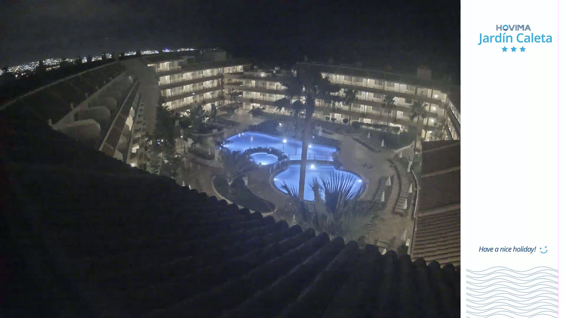 A nighttime aerial view shows a multi-story building complex surrounding a lit swimming pool area.