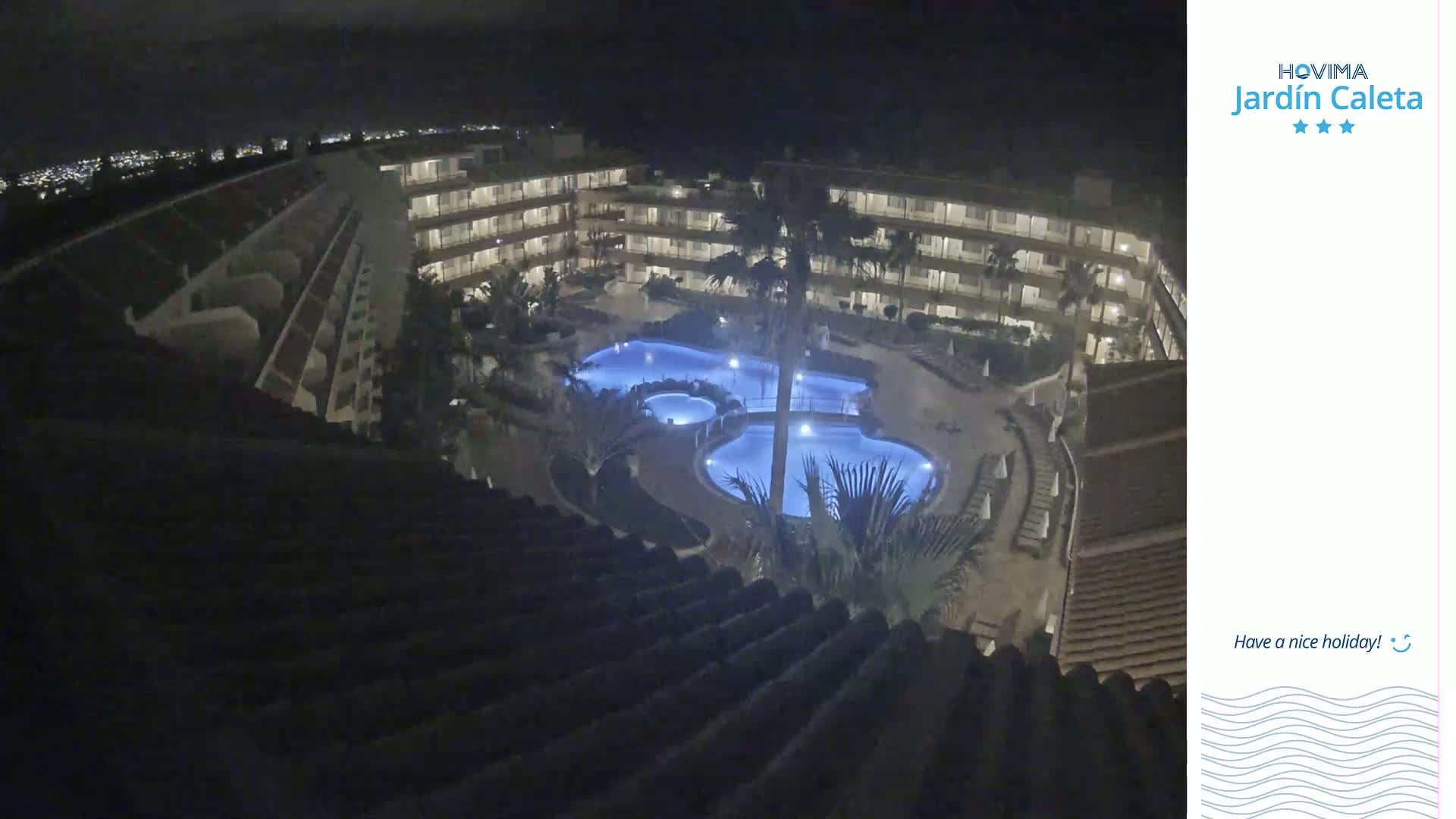 A nighttime aerial view shows a multi-story building complex surrounding a lit pool area.