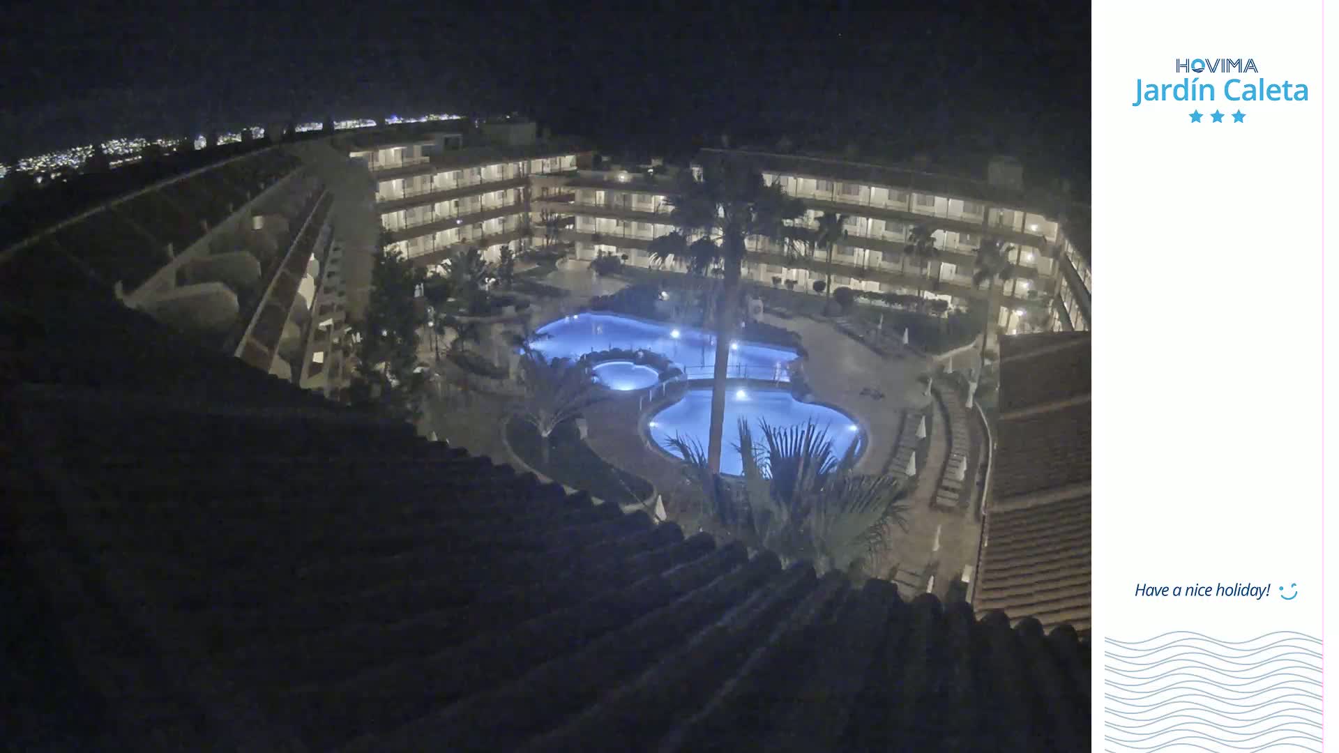 At night, a multi-story building surrounds a lit, irregularly shaped swimming pool complex.