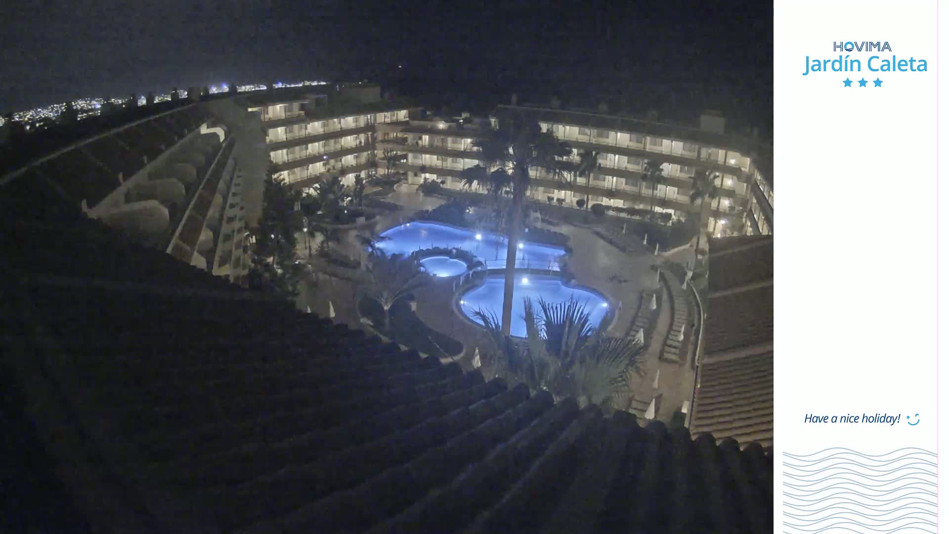 A nighttime aerial view of a multi-story building complex with multiple pools illuminated in blue.