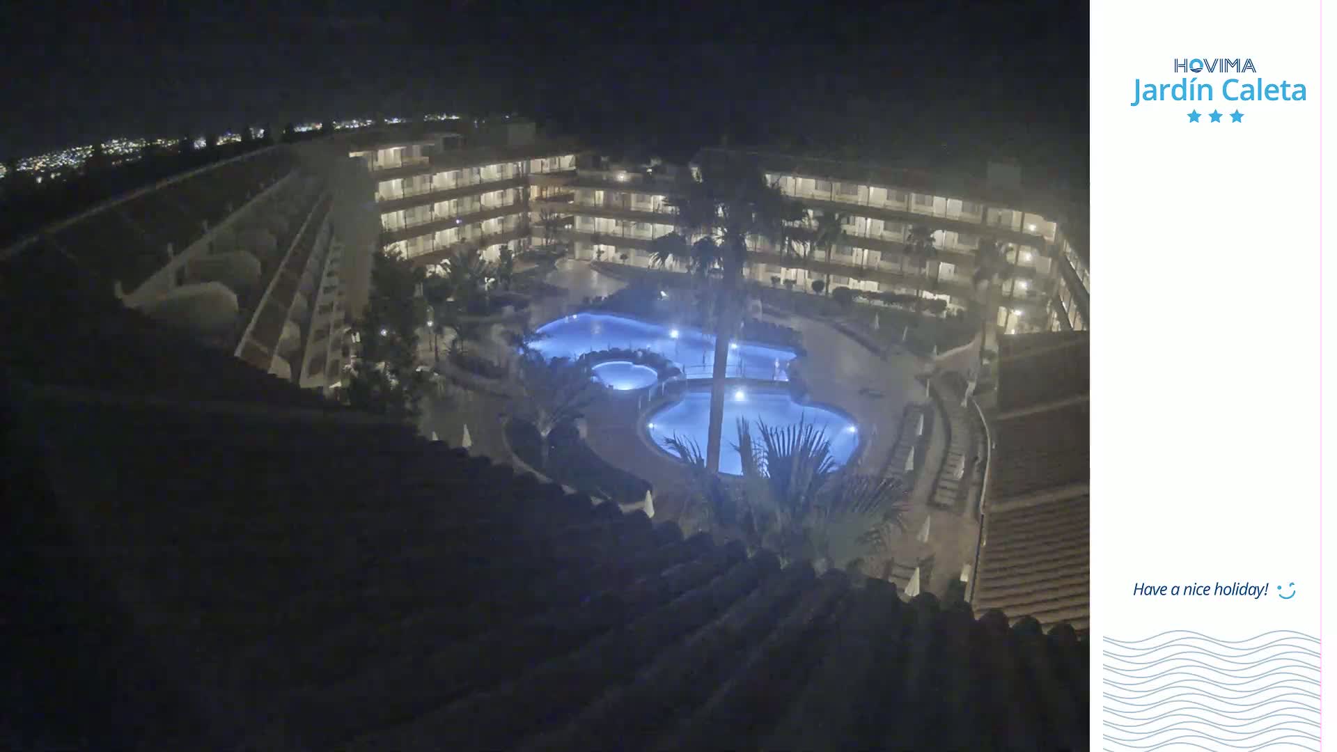 A nighttime aerial view shows a multi-story building complex surrounding a lit swimming pool area.