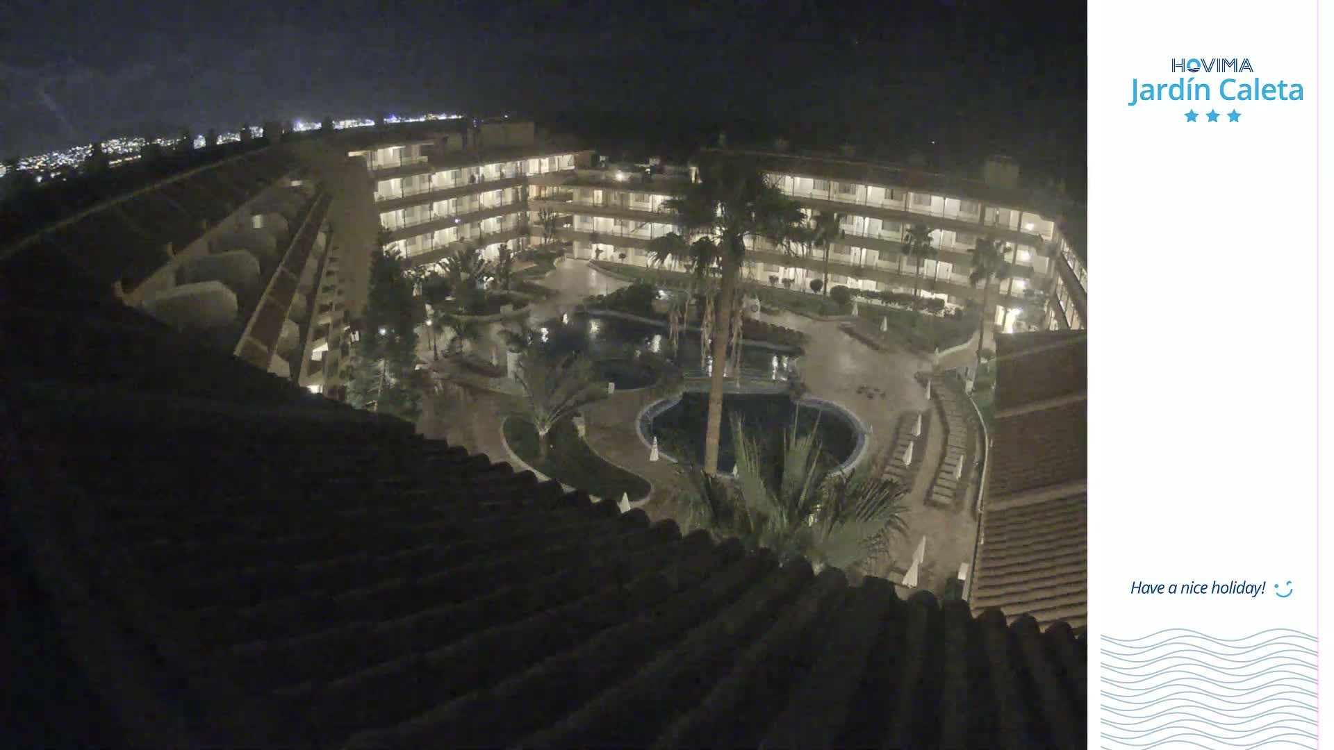 A nighttime aerial view of a multi-story building complex surrounding a courtyard with pools and palm trees.
