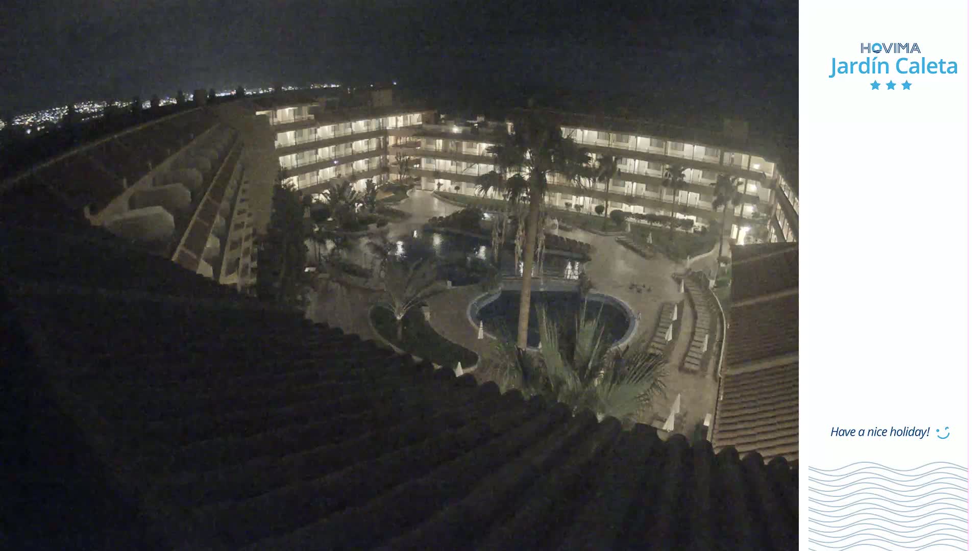 A nighttime aerial view shows a multi-story hotel complex surrounding a courtyard with pools and palm trees.