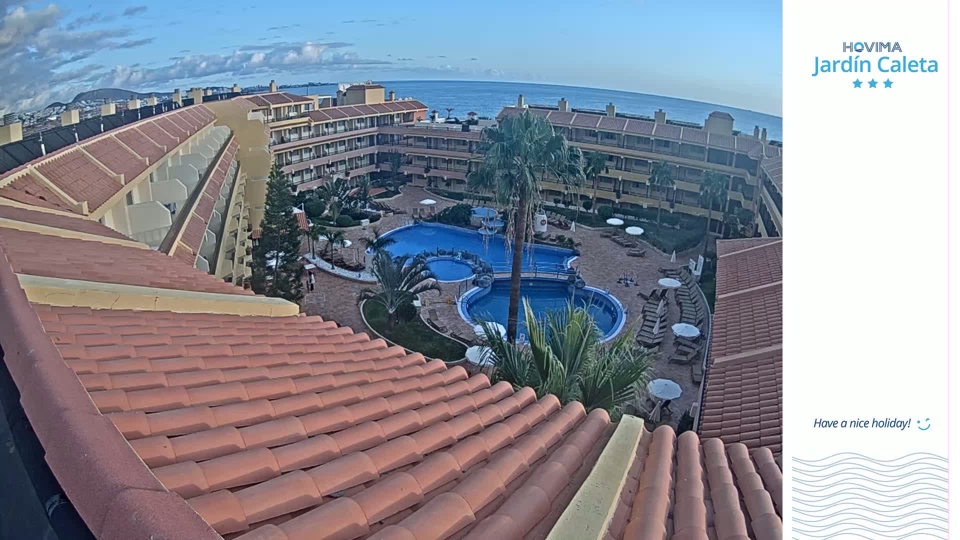 An aerial view shows a resort with a large pool complex under a mostly clear sky.