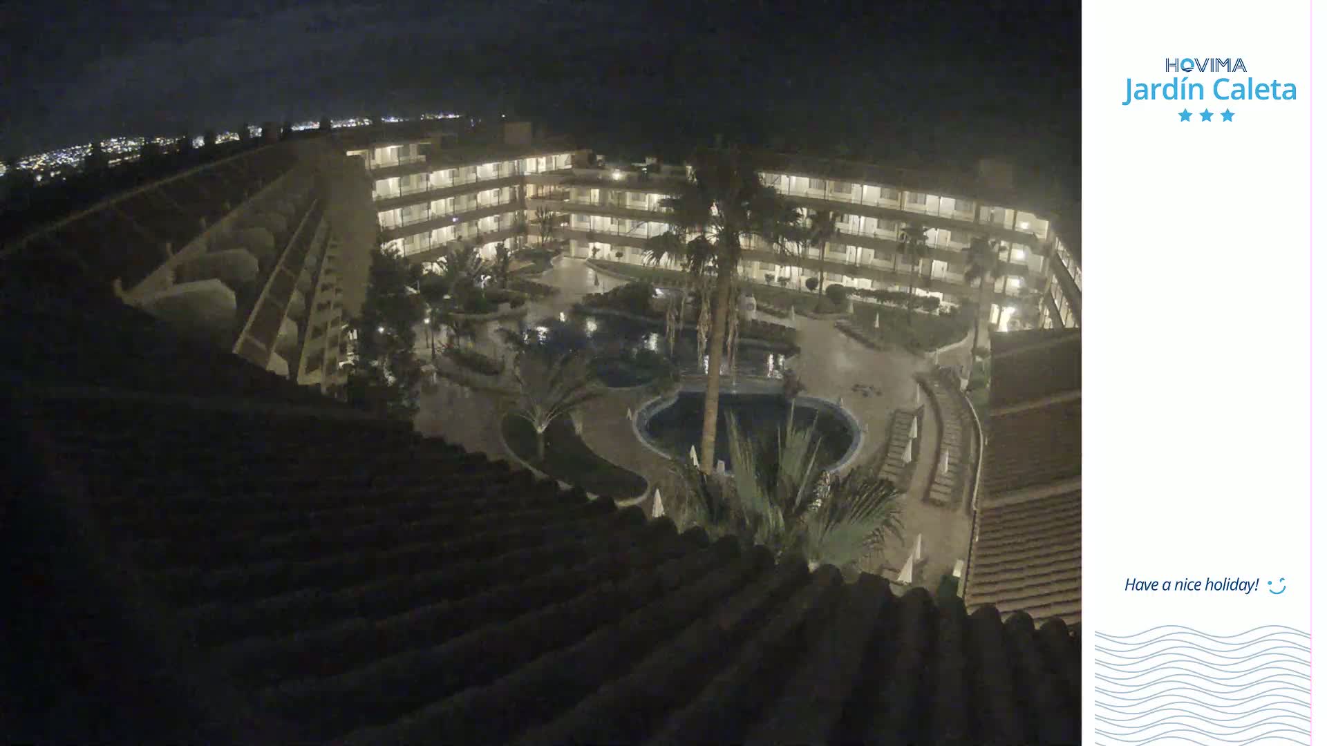 A nighttime aerial view of a multi-story hotel complex with surrounding landscaping, including palm trees and swimming pools.