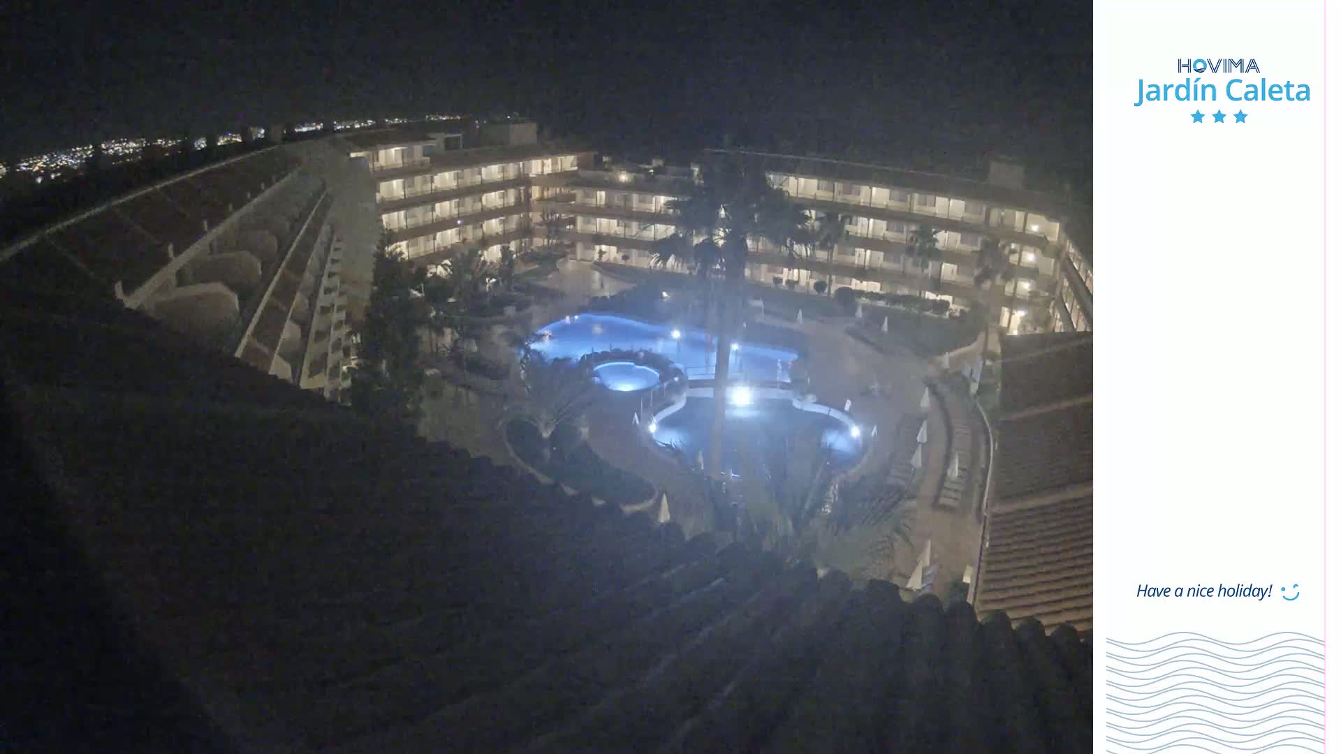 A nighttime aerial view of a multi-story hotel complex surrounding a lit pool.