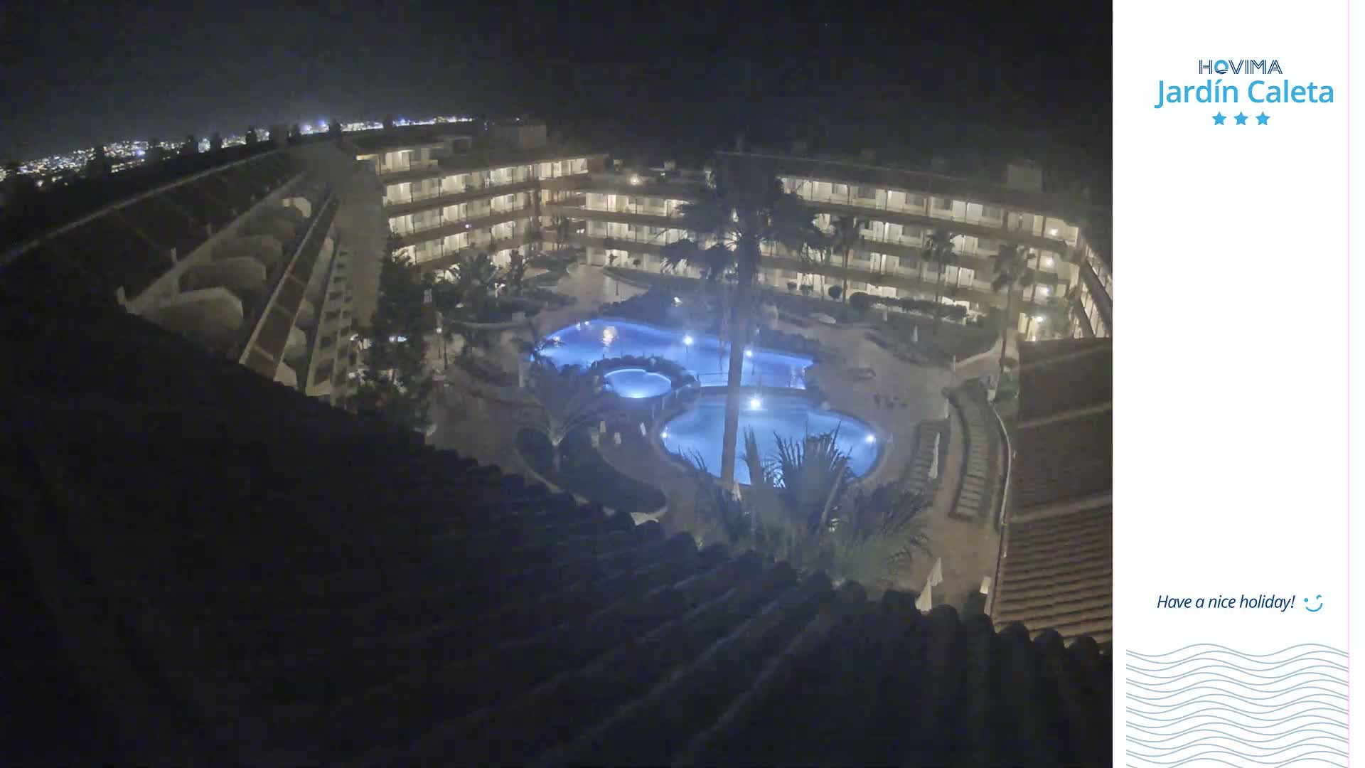 A nighttime aerial view shows a multi-story building complex surrounding a lit swimming pool area.