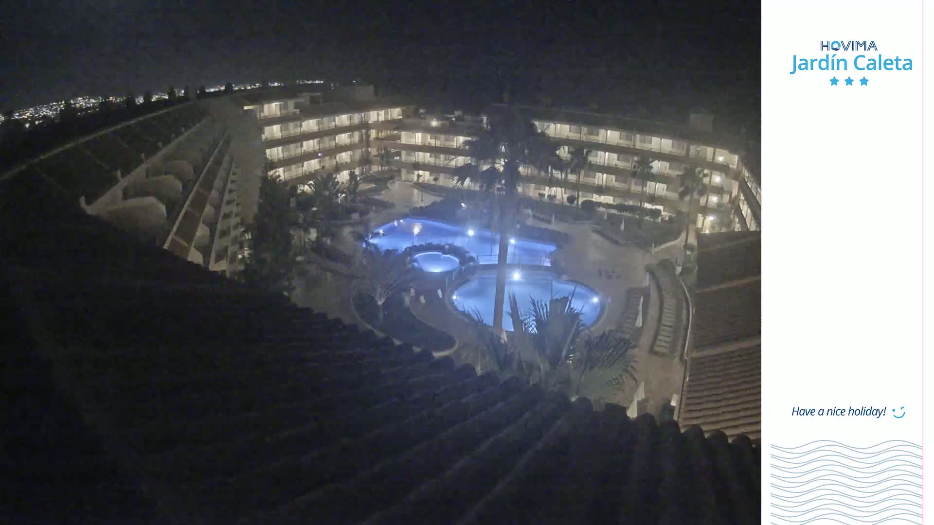 A nighttime, overhead view of a multi-story building complex surrounding several illuminated swimming pools.