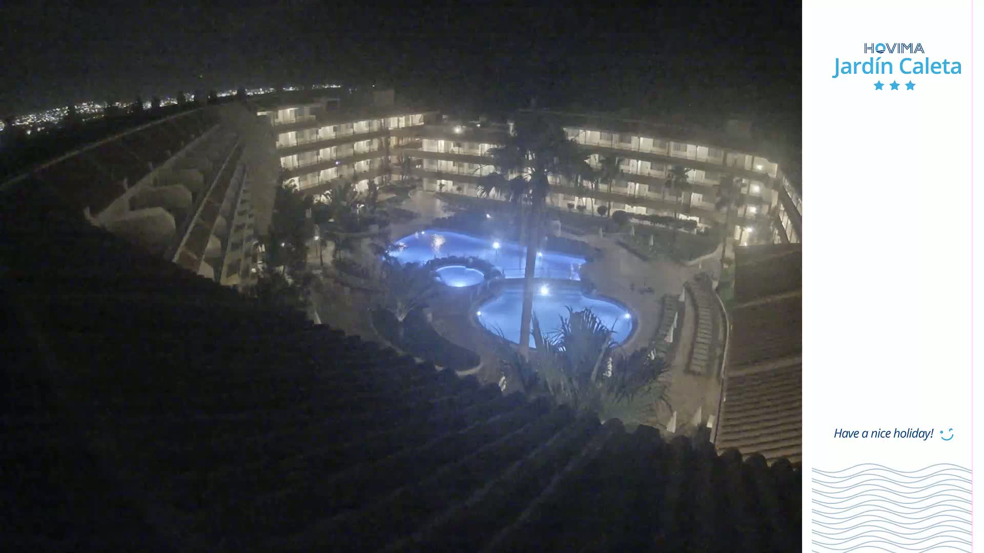 A nighttime aerial view shows a multi-story building complex surrounding a lit swimming pool.