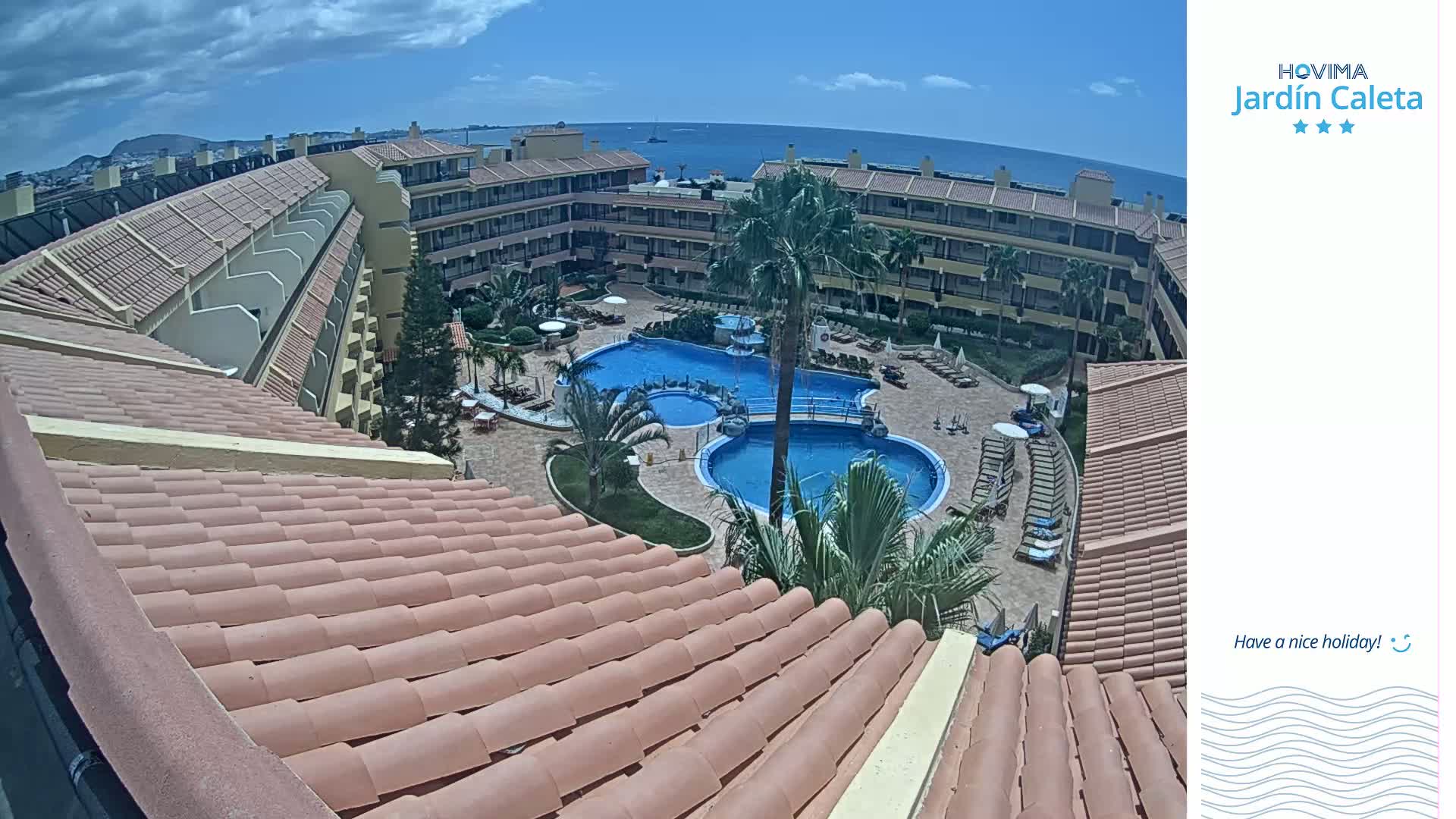 An overhead view shows a resort pool area with multiple pools and surrounding buildings under a partly cloudy sky.