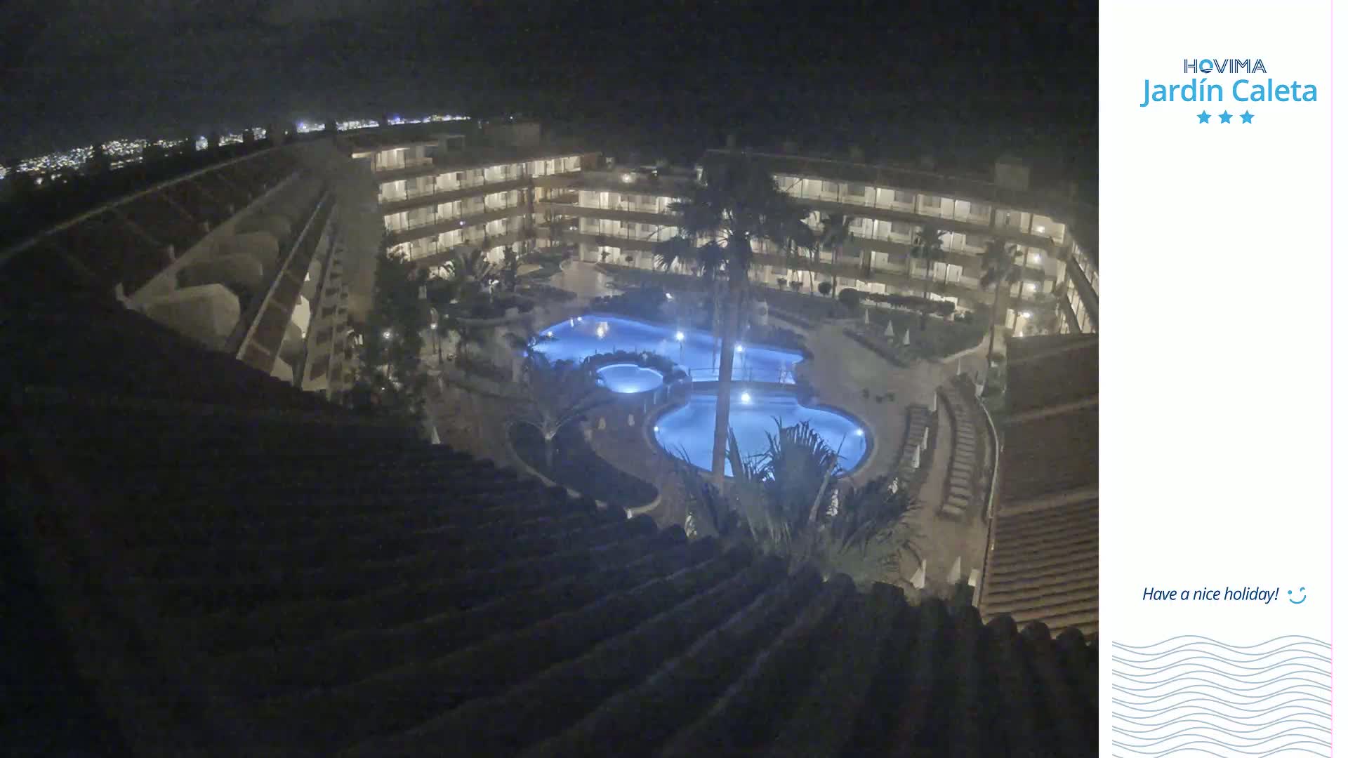 A nighttime aerial view shows a multi-story building complex surrounding a lit swimming pool.