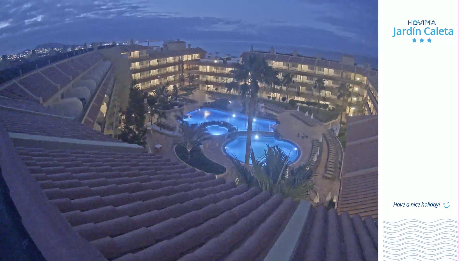 An illuminated apartment complex with a swimming pool is seen at night under a dark, cloudy sky.