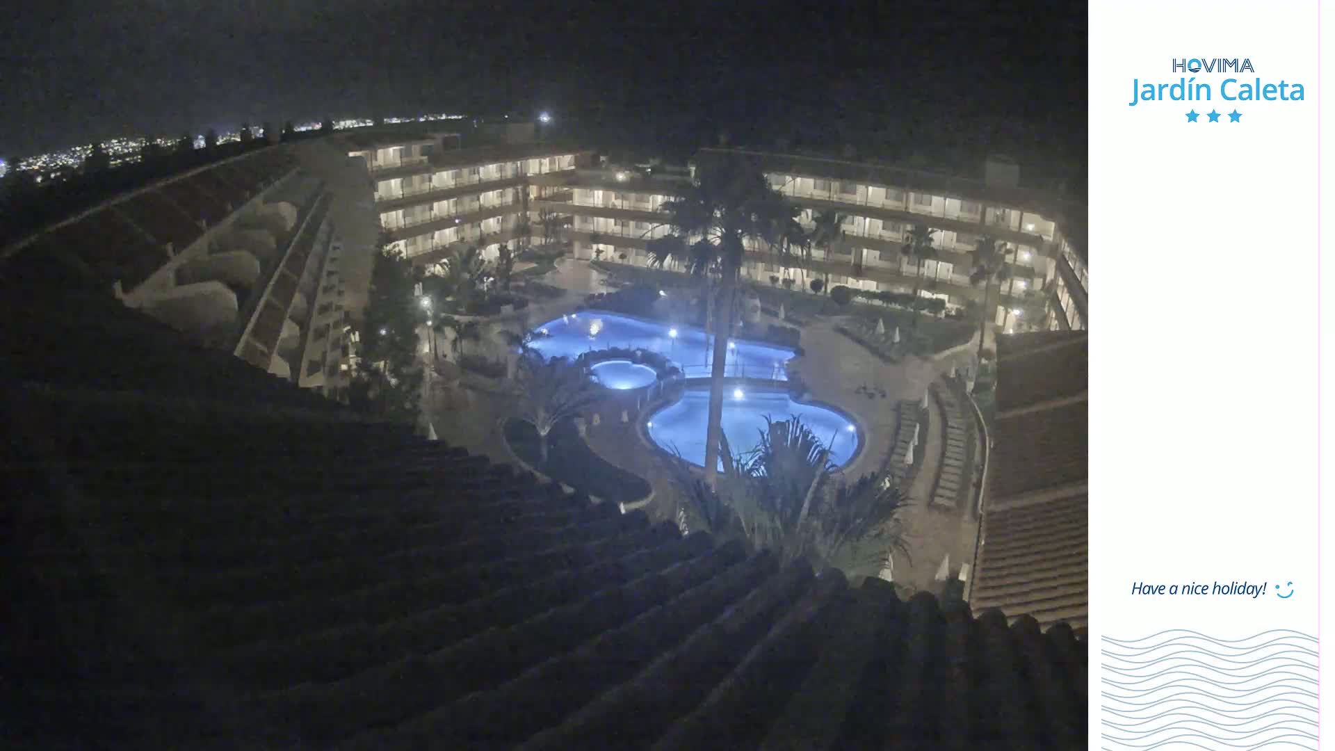 A nighttime aerial view shows a multi-story building complex surrounding a lit swimming pool.