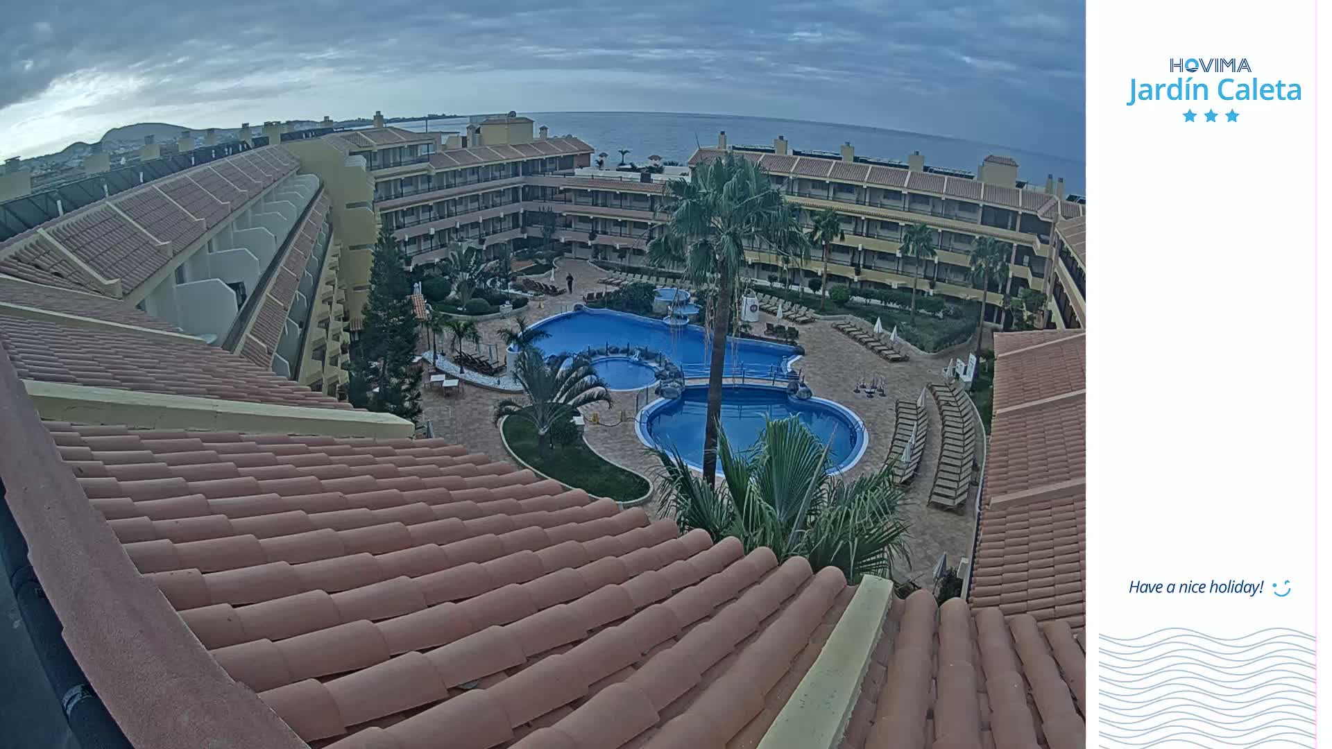 An overhead view of a resort complex with a large pool and surrounding buildings under an overcast sky.