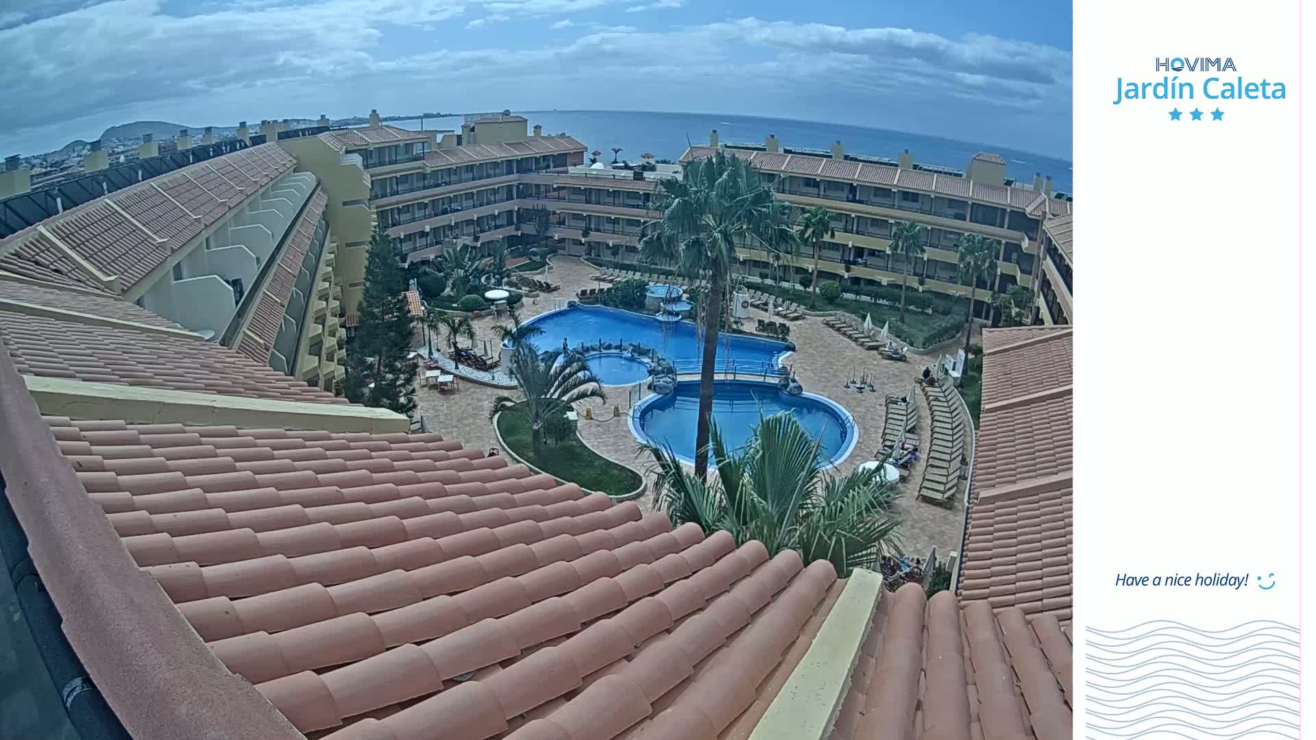 An overhead view of a resort with a large pool and surrounding buildings on a partly cloudy day.