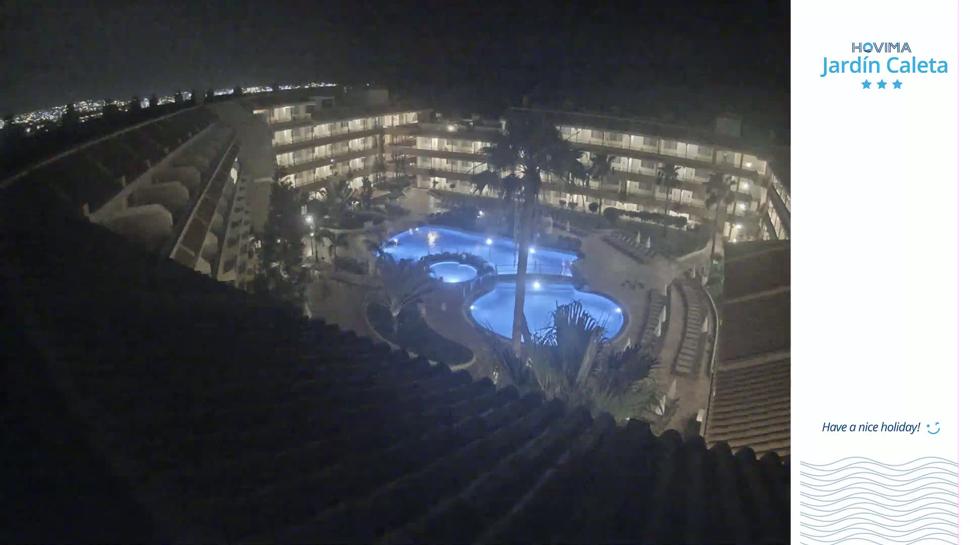 A nighttime aerial view shows a multi-story building complex surrounding a lit swimming pool.