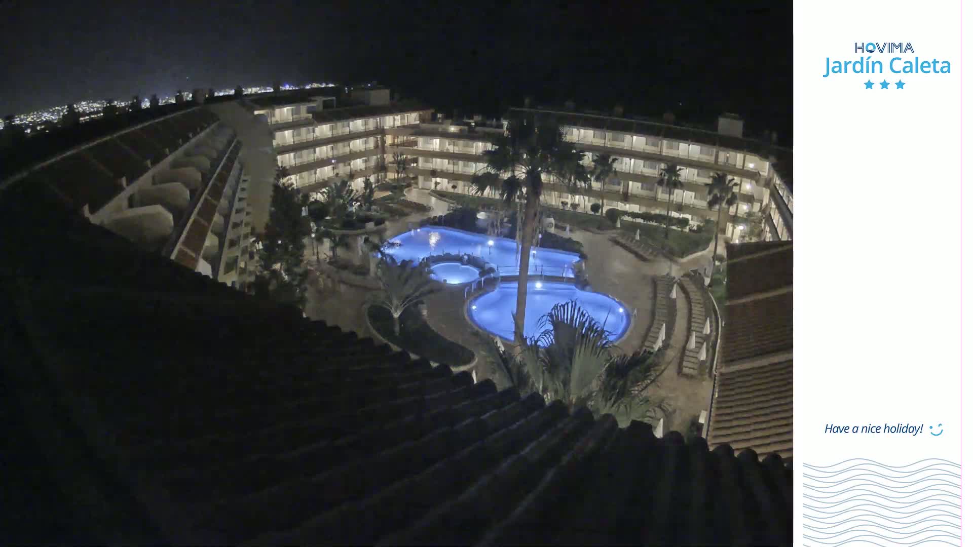 A nighttime, high-angle view shows a multi-story hotel complex surrounding a lit, kidney-shaped swimming pool.