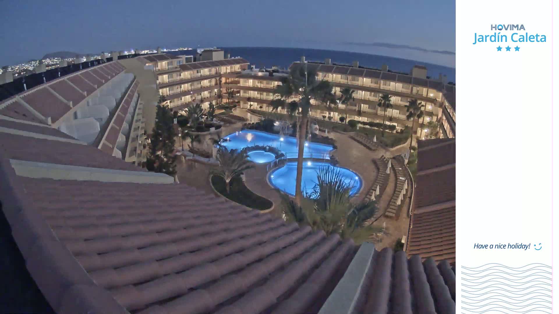 An illuminated, multi-level hotel complex with a large swimming pool, viewed at night under a dark sky.