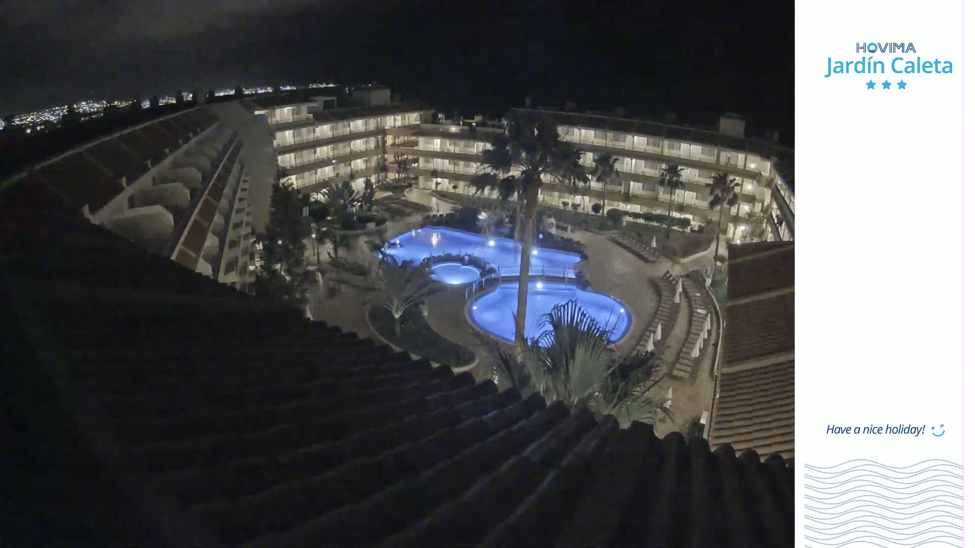 A nighttime aerial view shows a multi-story building complex surrounding a lit-up swimming pool area.