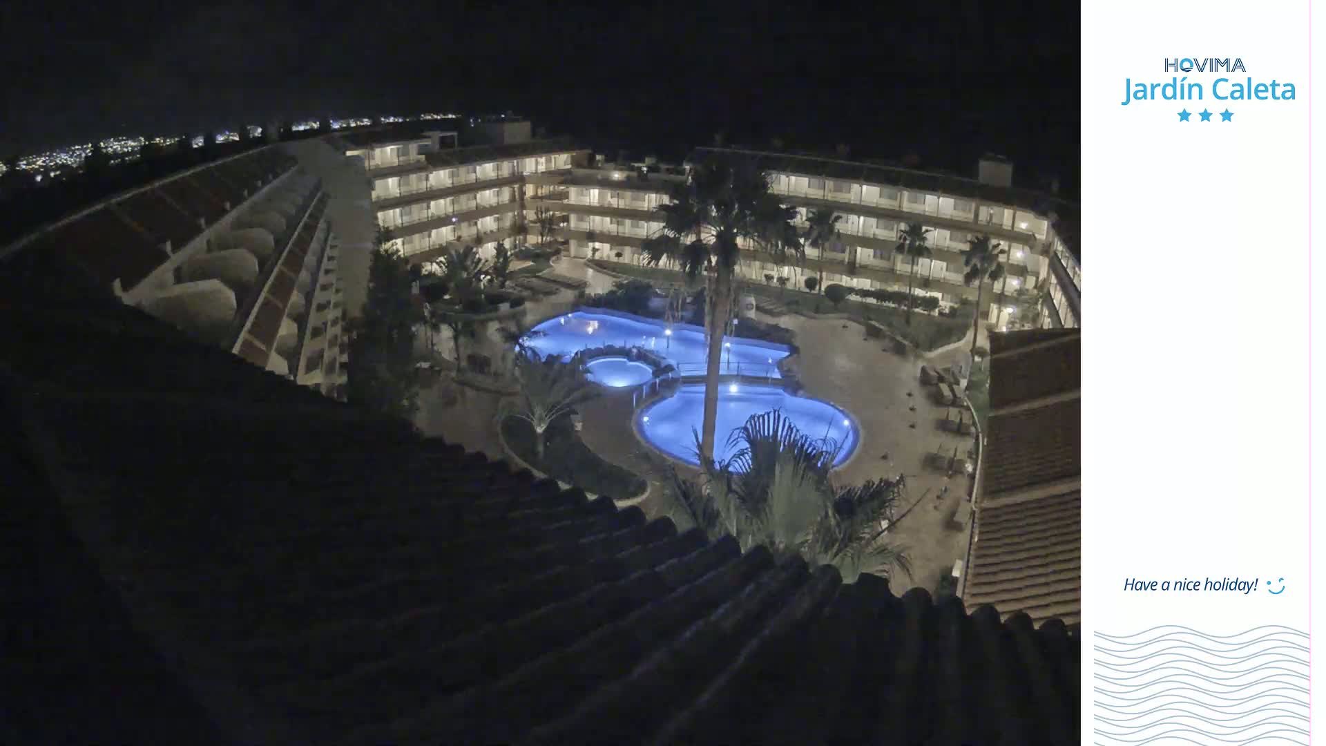An illuminated resort complex with multiple pools is seen at night.