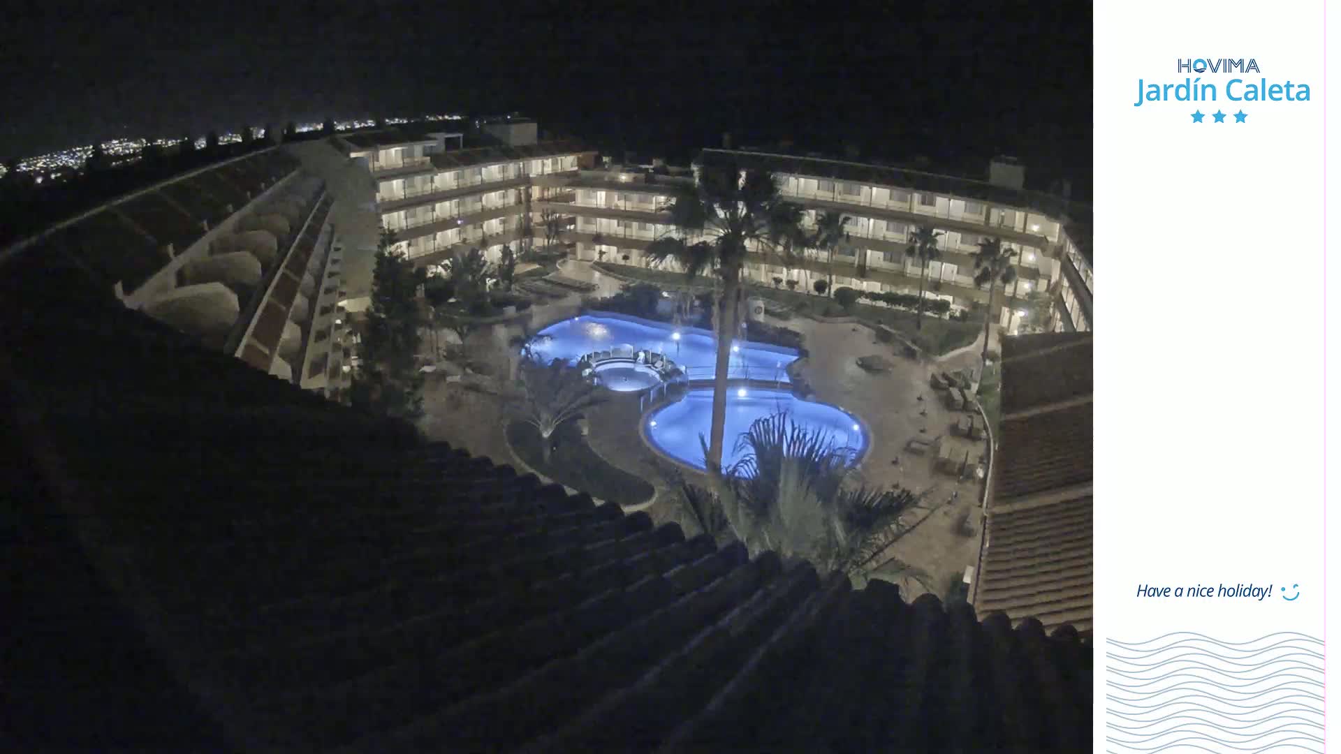 A nighttime aerial view shows a multi-story building complex surrounding a lit swimming pool.