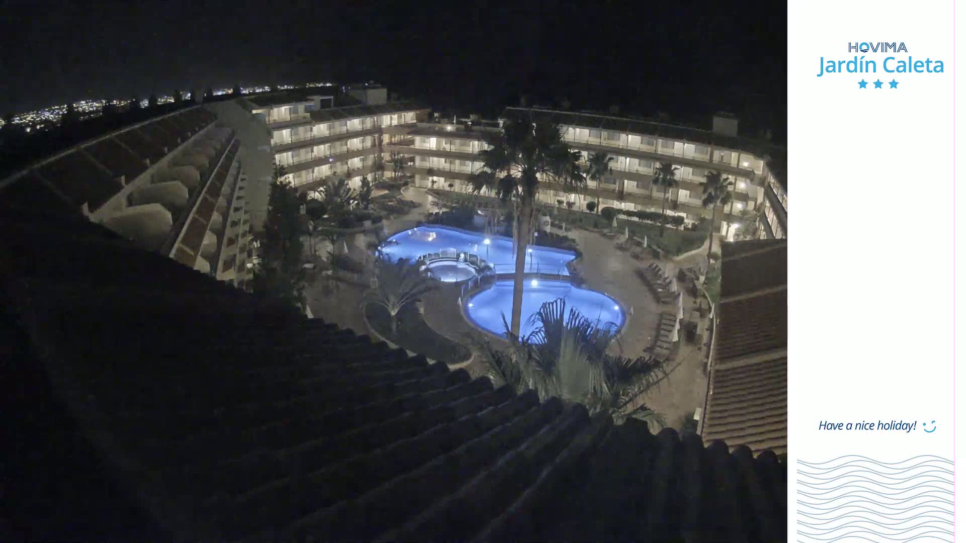 A nighttime, overhead view of a multi-story hotel complex surrounding a lit swimming pool.