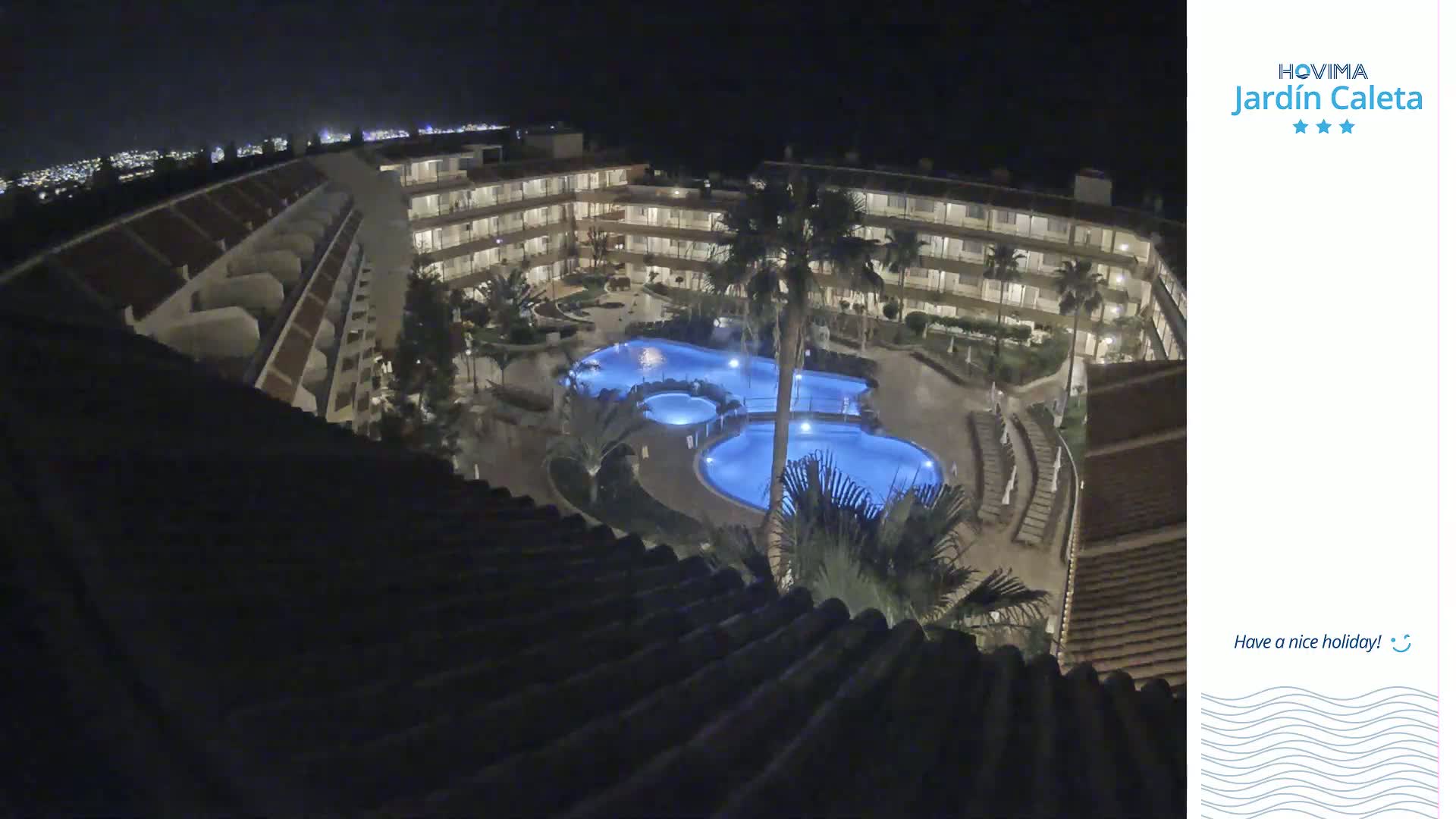 An illuminated outdoor pool complex is surrounded by a multi-story building at night.