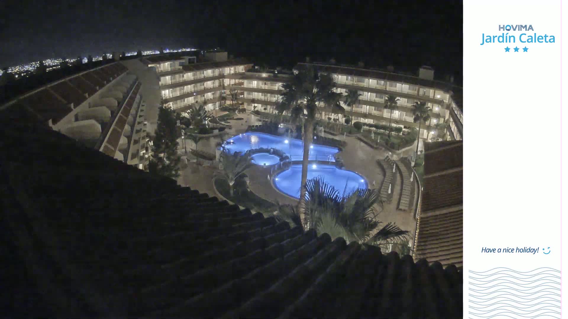 A nighttime aerial view shows a multi-story building complex surrounding a lit swimming pool area.