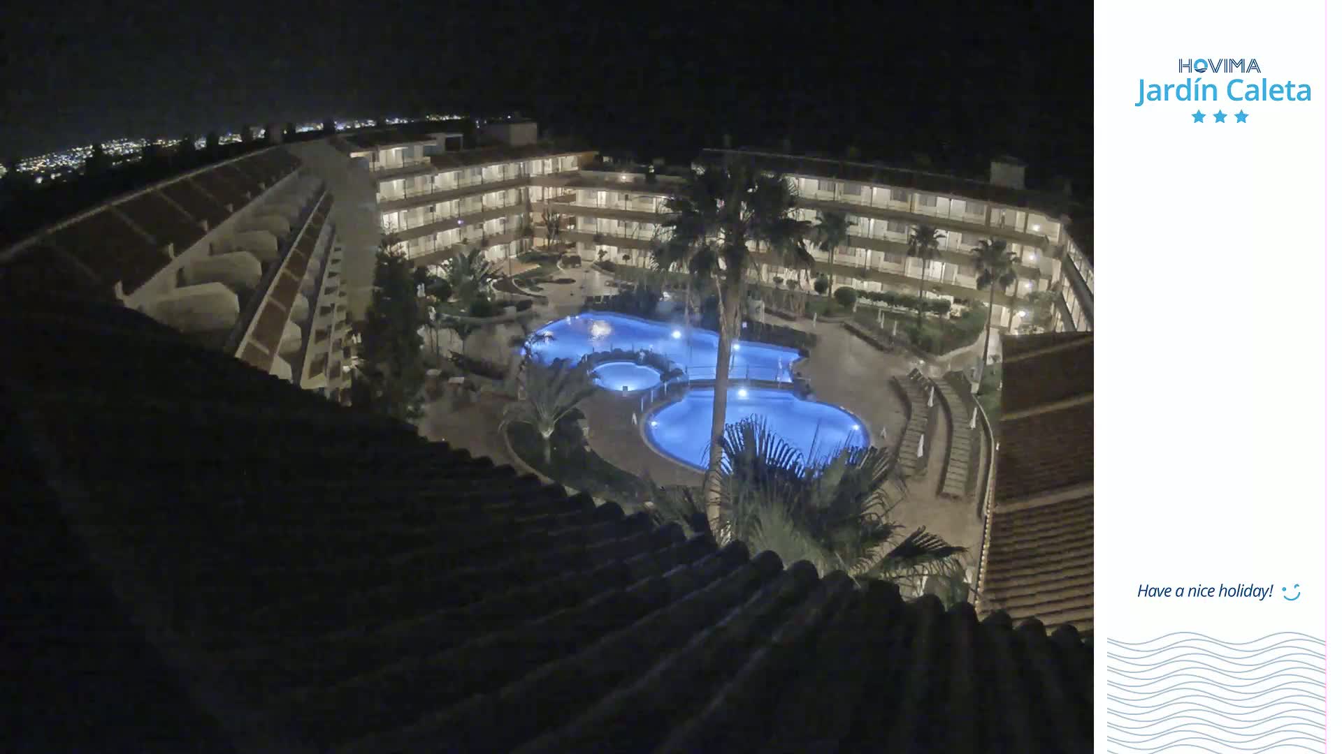 At night, a multi-story building surrounds a lit, irregularly shaped swimming pool complex.