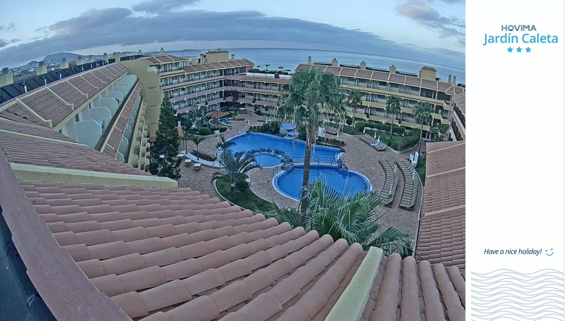 An overhead view shows a resort pool area with multiple buildings under an overcast sky.