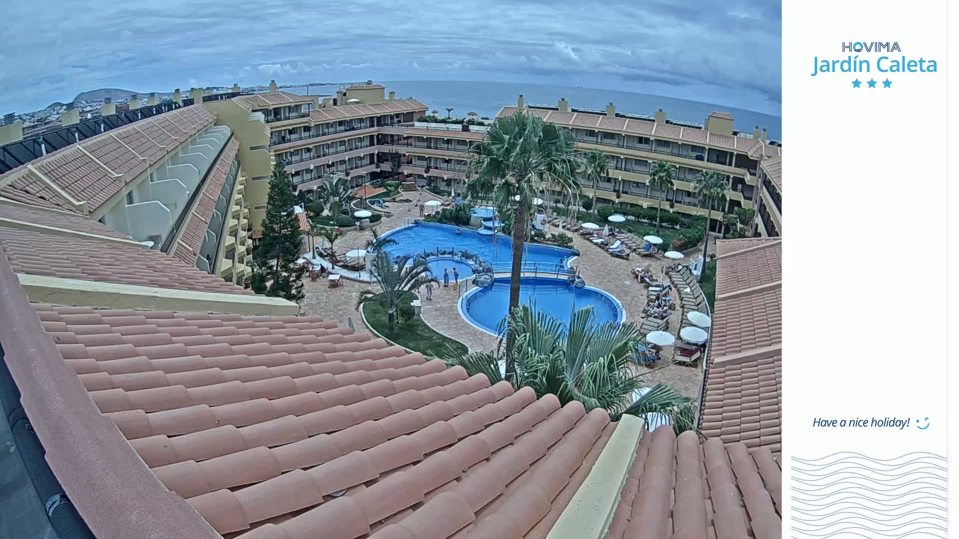An overhead view of a resort complex with multiple pools and lounge chairs, under partly cloudy skies.