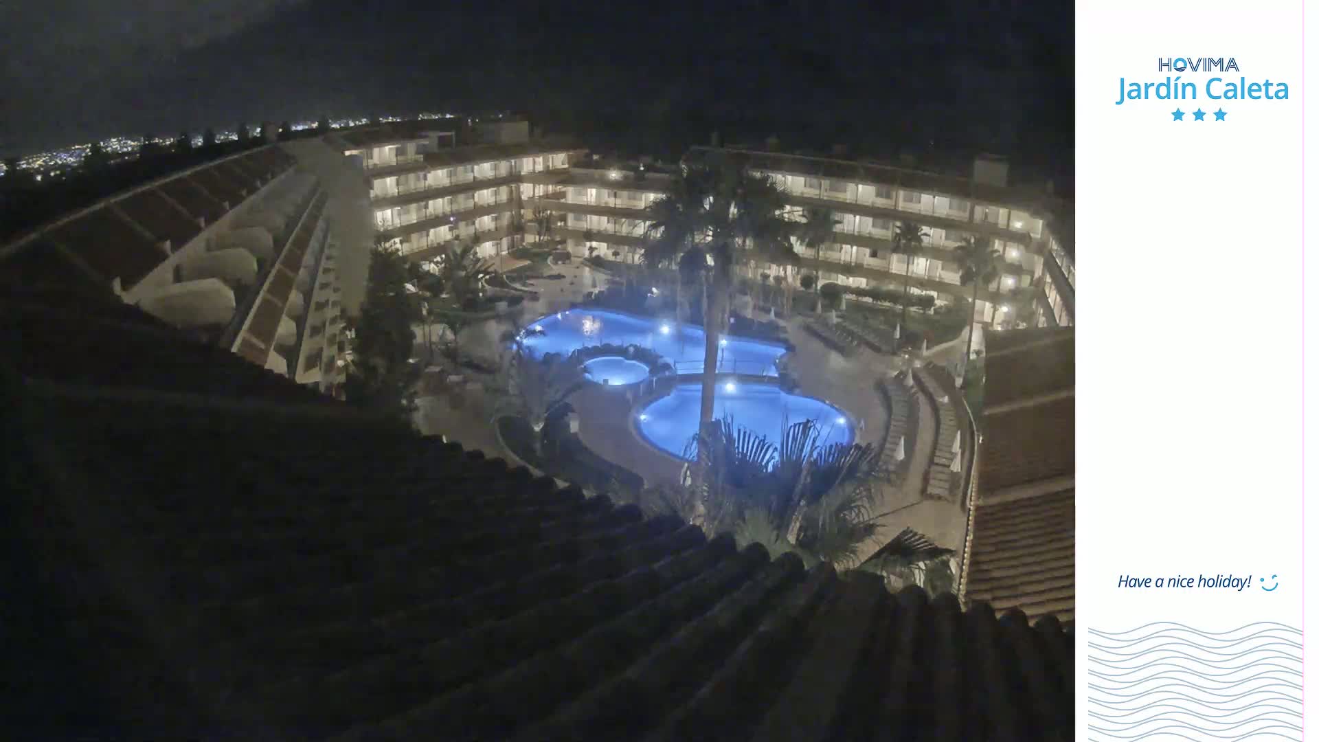 A nighttime aerial view shows a multi-story building complex surrounding a lit swimming pool area.
