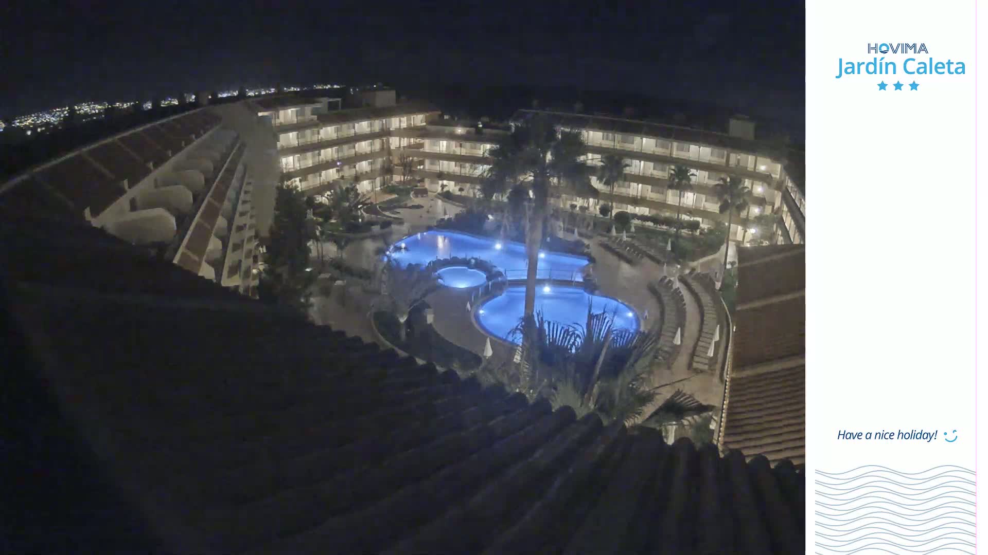 An illuminated, multi-level hotel complex at night surrounds a blue-lit pool area.