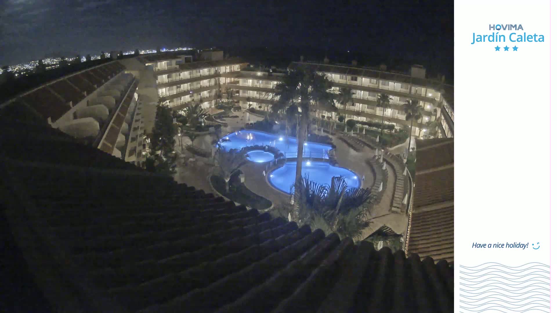 A nighttime aerial view shows a multi-story building complex surrounding a lit swimming pool area.