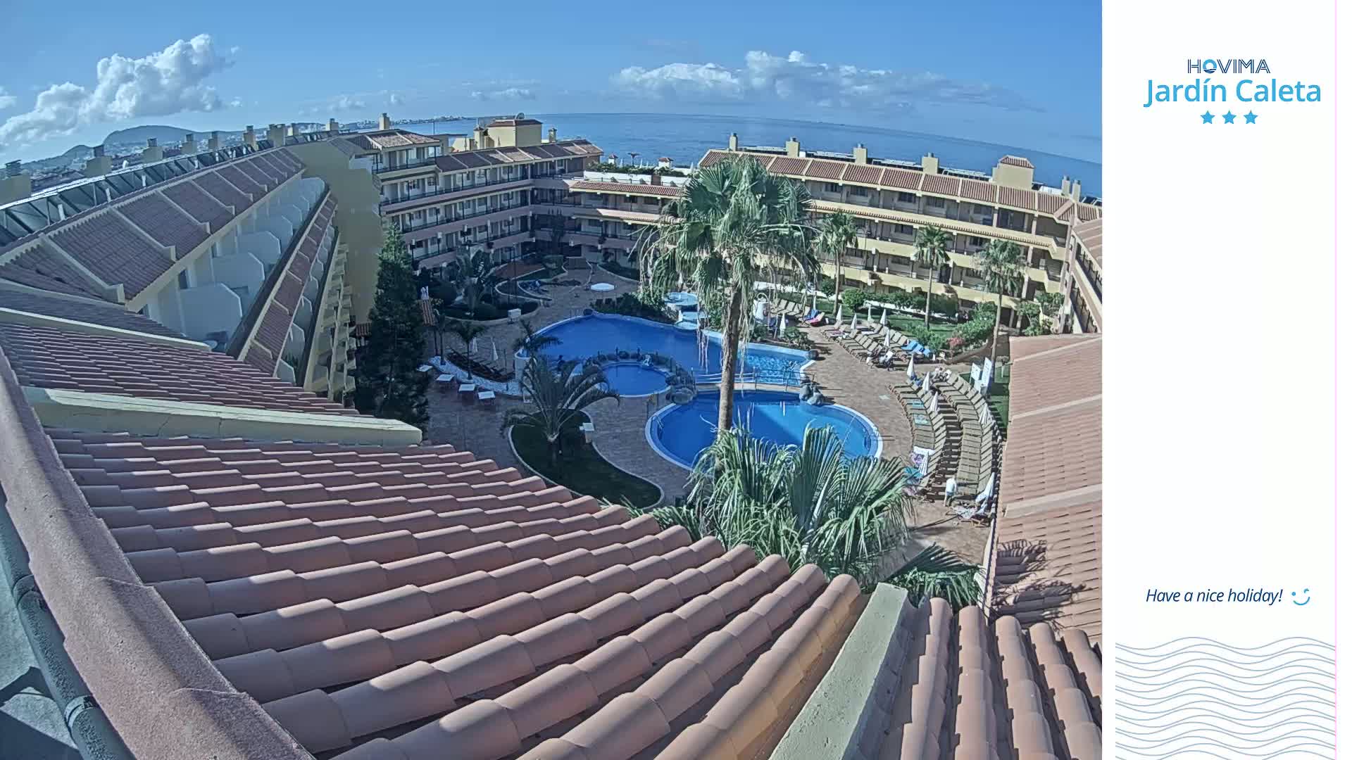 A sunny day overlooking a resort with multiple buildings surrounding a large pool and a view of the ocean in the distance.
