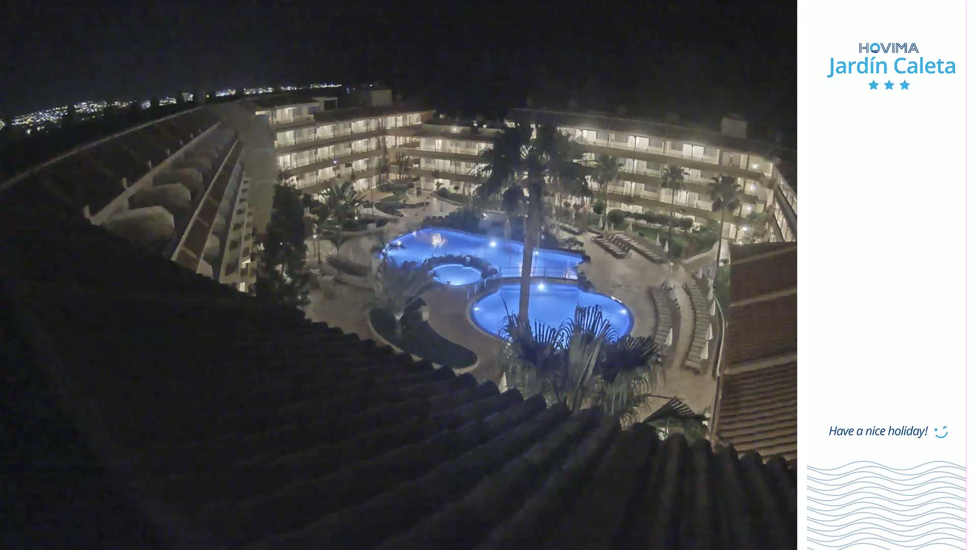 At night, a multi-story building surrounds a lit swimming pool complex.